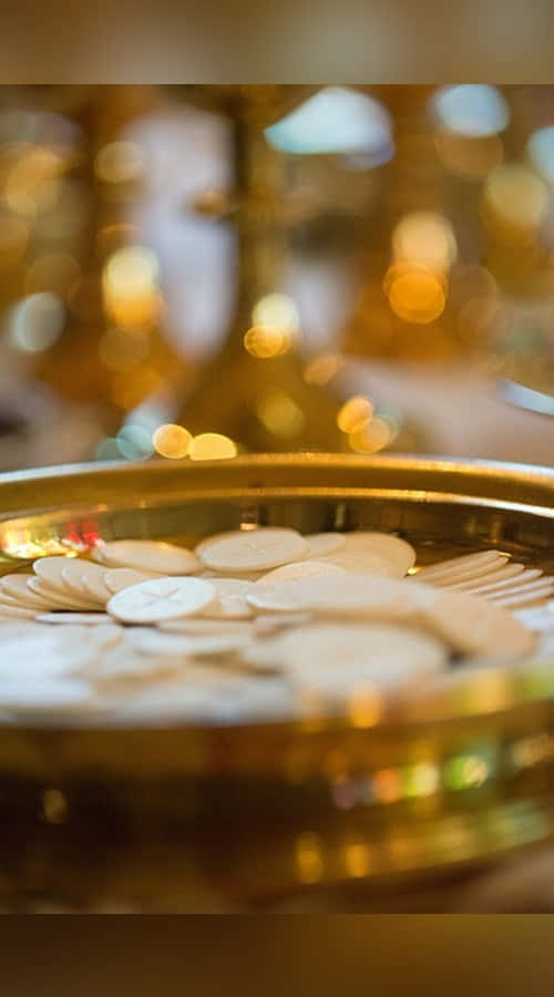 Sacrament 桌布 壁紙 — 淺景深捕捉到金色托盤上的白色聖體薄餅，背景是模糊的金色宗教物品。