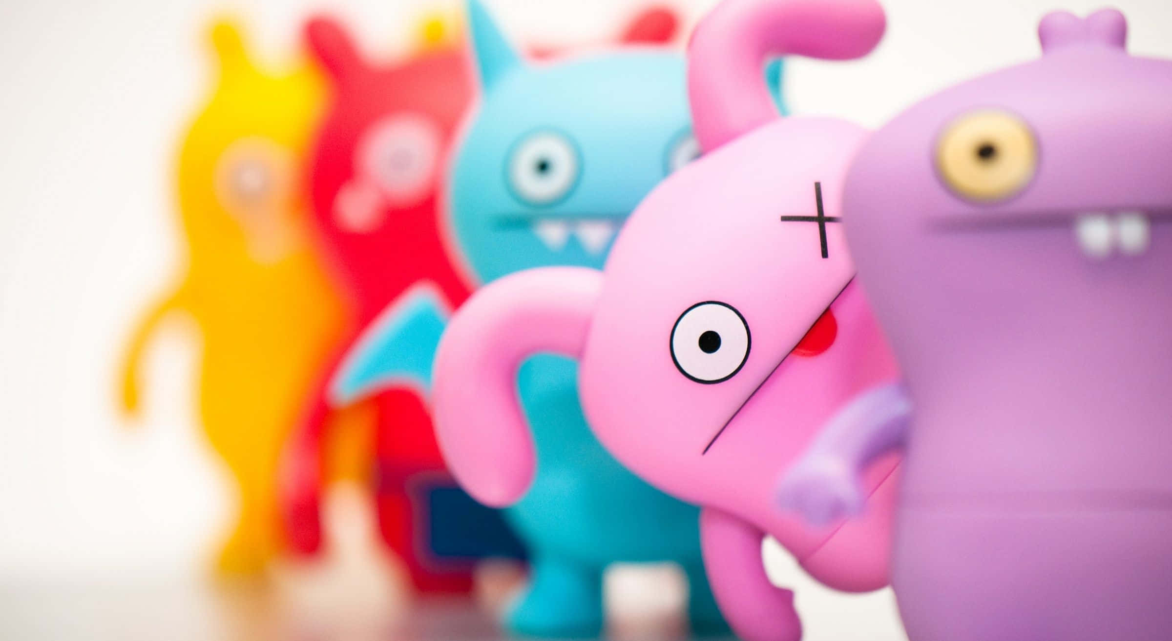 Cute HD 桌布 壁紙 — 淺景深突出了粉紅色Uglydoll玩具的鬥雞眼表情，而背景中色彩繽紛的Uglydoll人物則模糊不清。