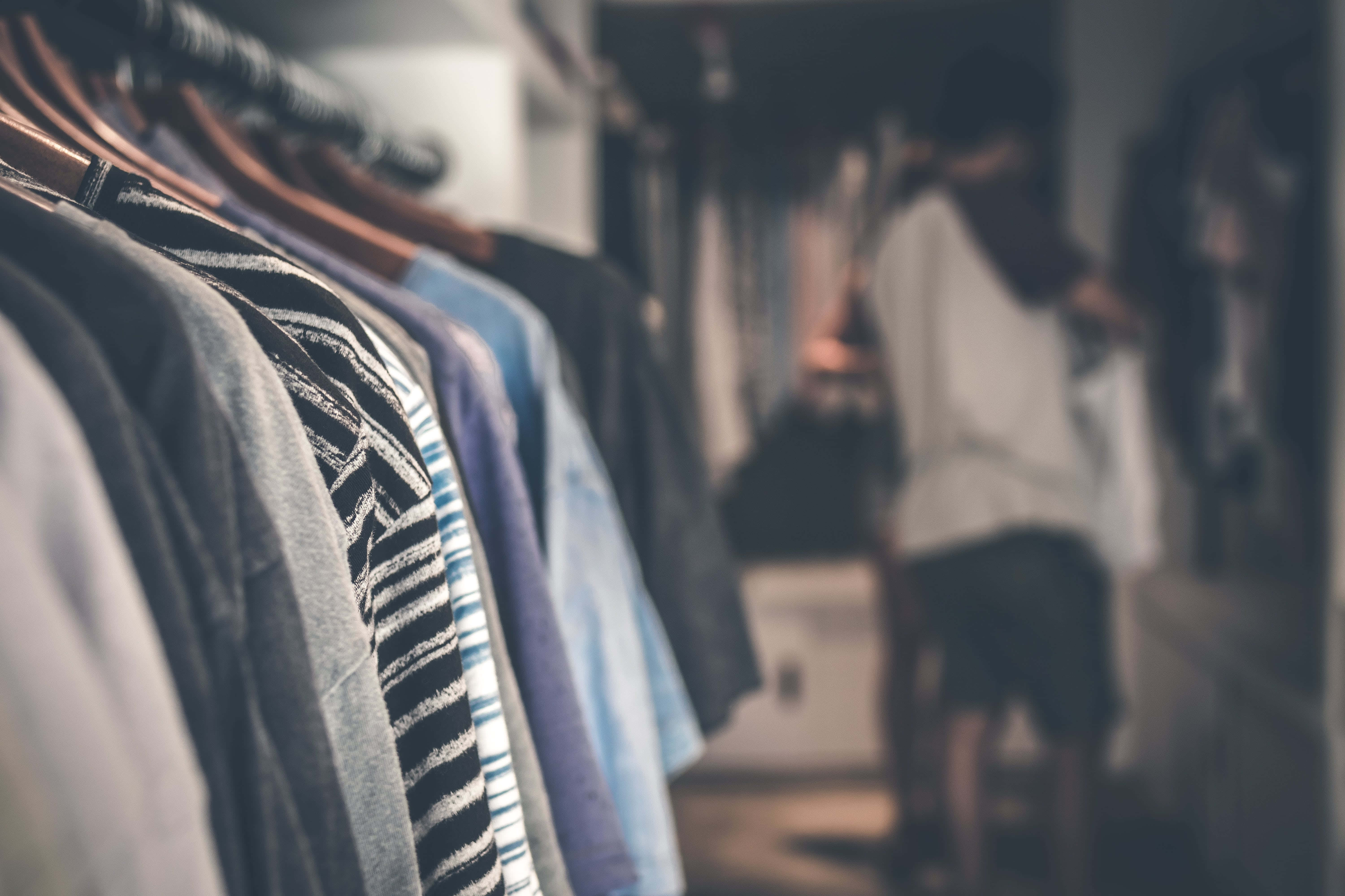 Clothes 桌布 壁紙 — 淺景深聚焦在一排掛起的衣服上，背景中一個模糊的人正在瀏覽。