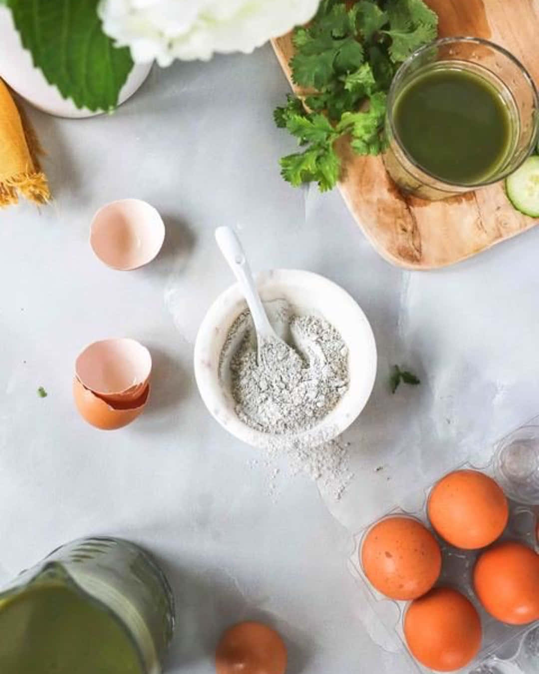 Eggshell 桌布 壁紙 — 淺灰色枱面嘅俯視圖，有裂開嘅蛋殼、一碗灰色粉末、新鮮香草同一杯綠色果汁。