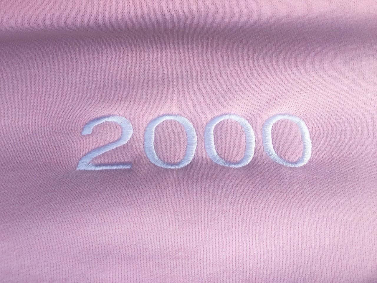 2000s 桌布 壁紙 — 淺紫色布料上白色刺繡「2000」數字的特寫，顯示質地和針腳細節。