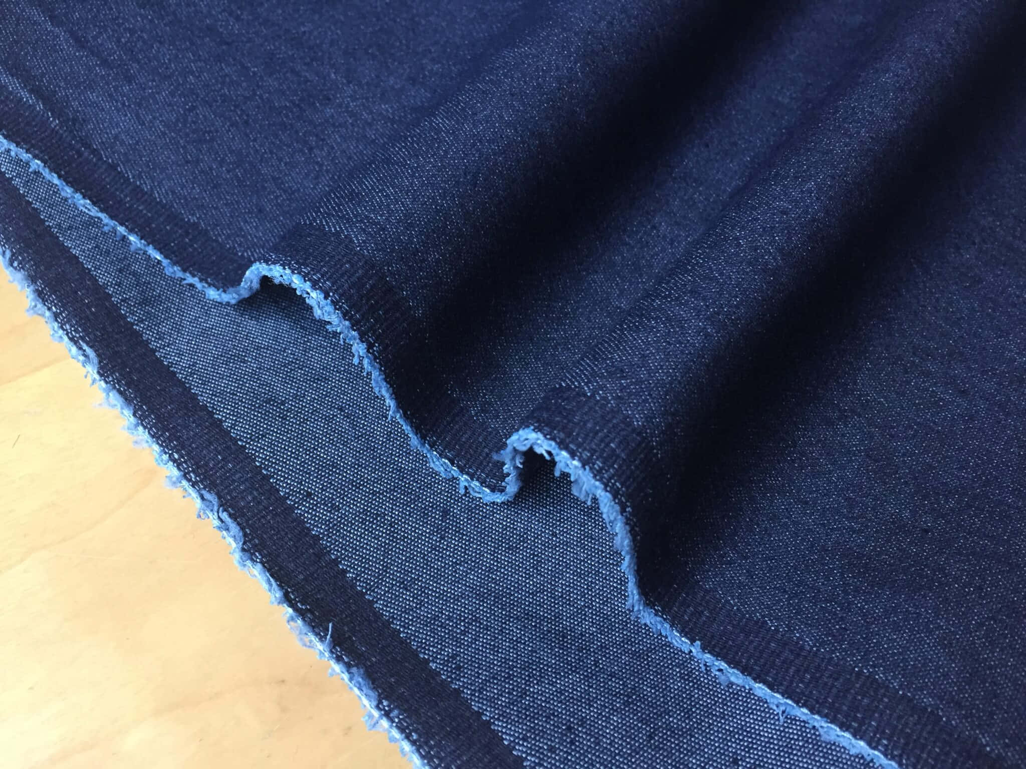 Denim Blue 桌布 壁紙 — 淺色木質表面上帶有磨損邊緣的質感深藍色牛仔布料的特寫。
