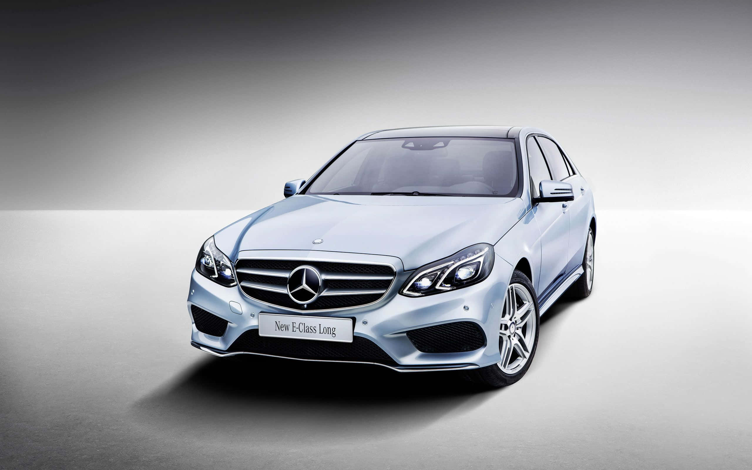 淺藍色梅賽德斯-奔馳 E 級 壁紙 — 一輛時尚的銀色 Mercedes-Benz E-Class Long 轎車在攝影棚燈光下，以極簡灰色漸變背景襯托，閃閃發光。