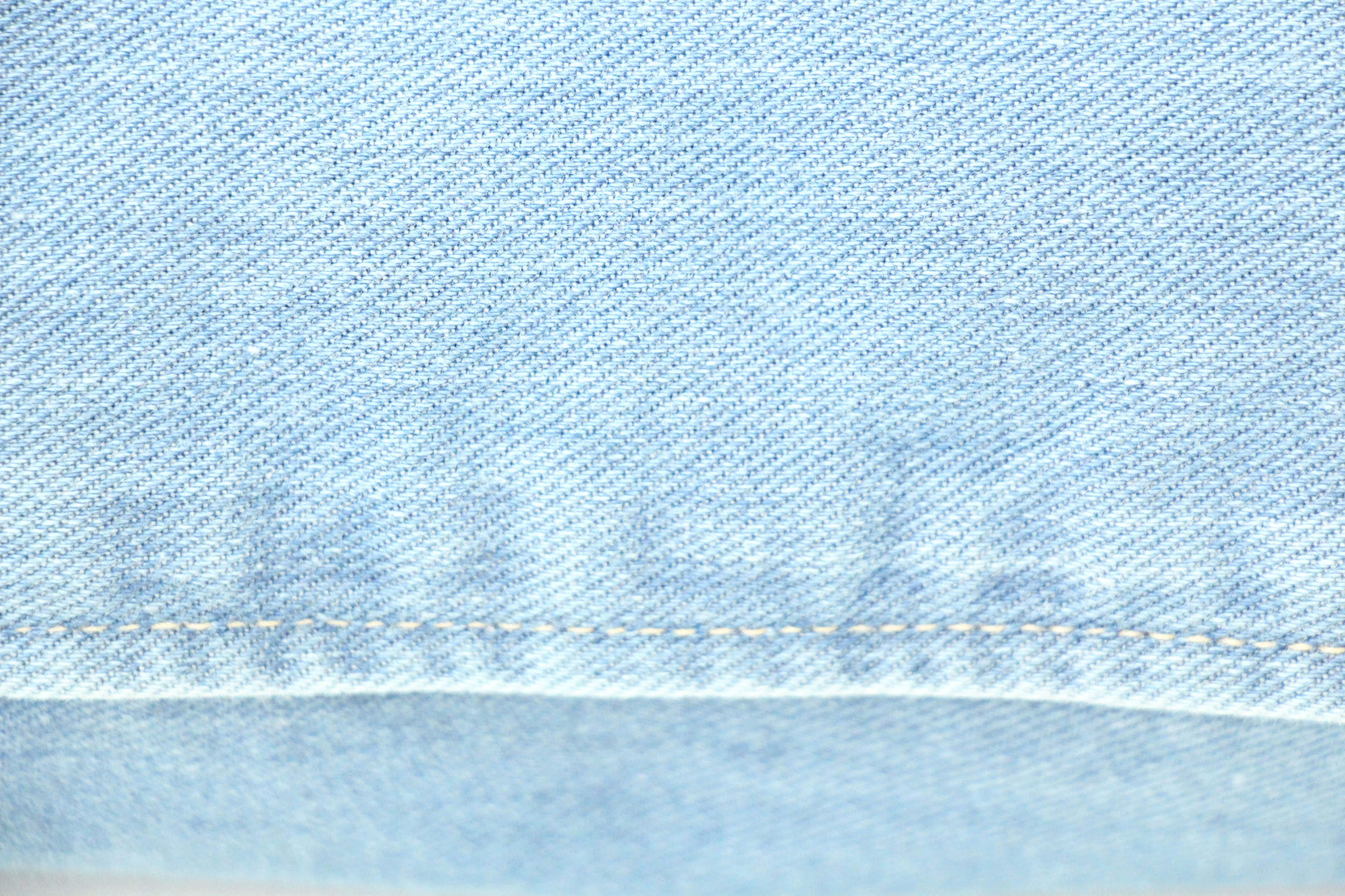 Denim 桌布 壁紙 — 淺藍色牛仔布料的特寫，顯示編織紋理和對比鮮明的黃色縫線。