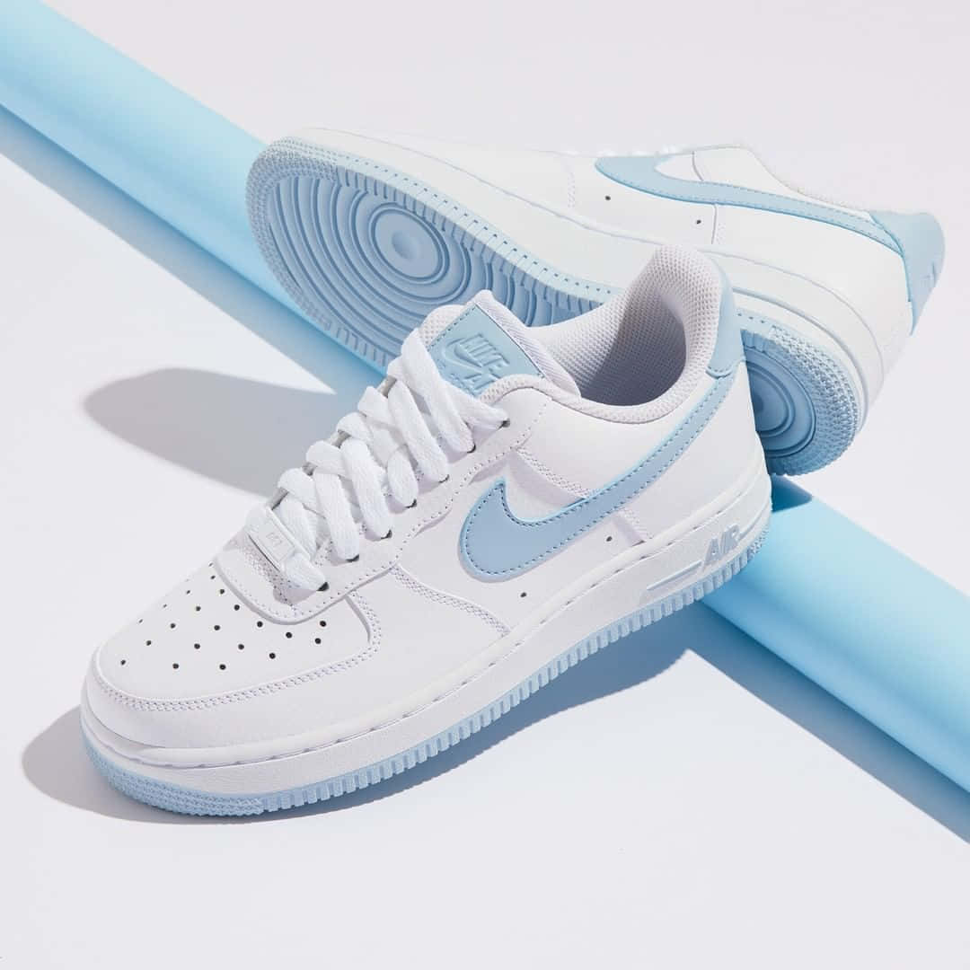 白色Nike Air Force 1運動鞋，帶有淺藍色細節，置於藍色圓柱體和白色表面上。
