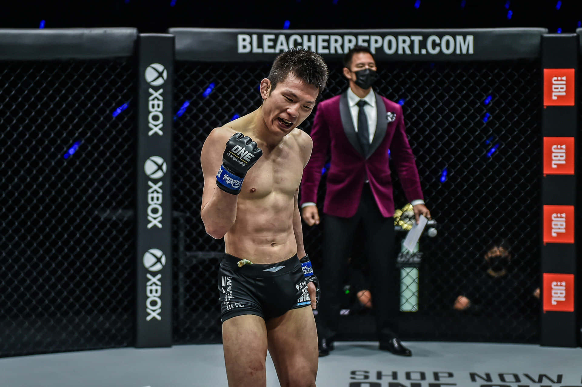 MMA拳手在八角籠內慶祝勝利，身後有贊助商標誌和一名官員。