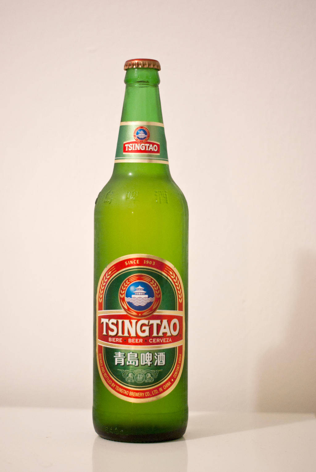 白色表面上的綠色青島啤酒瓶