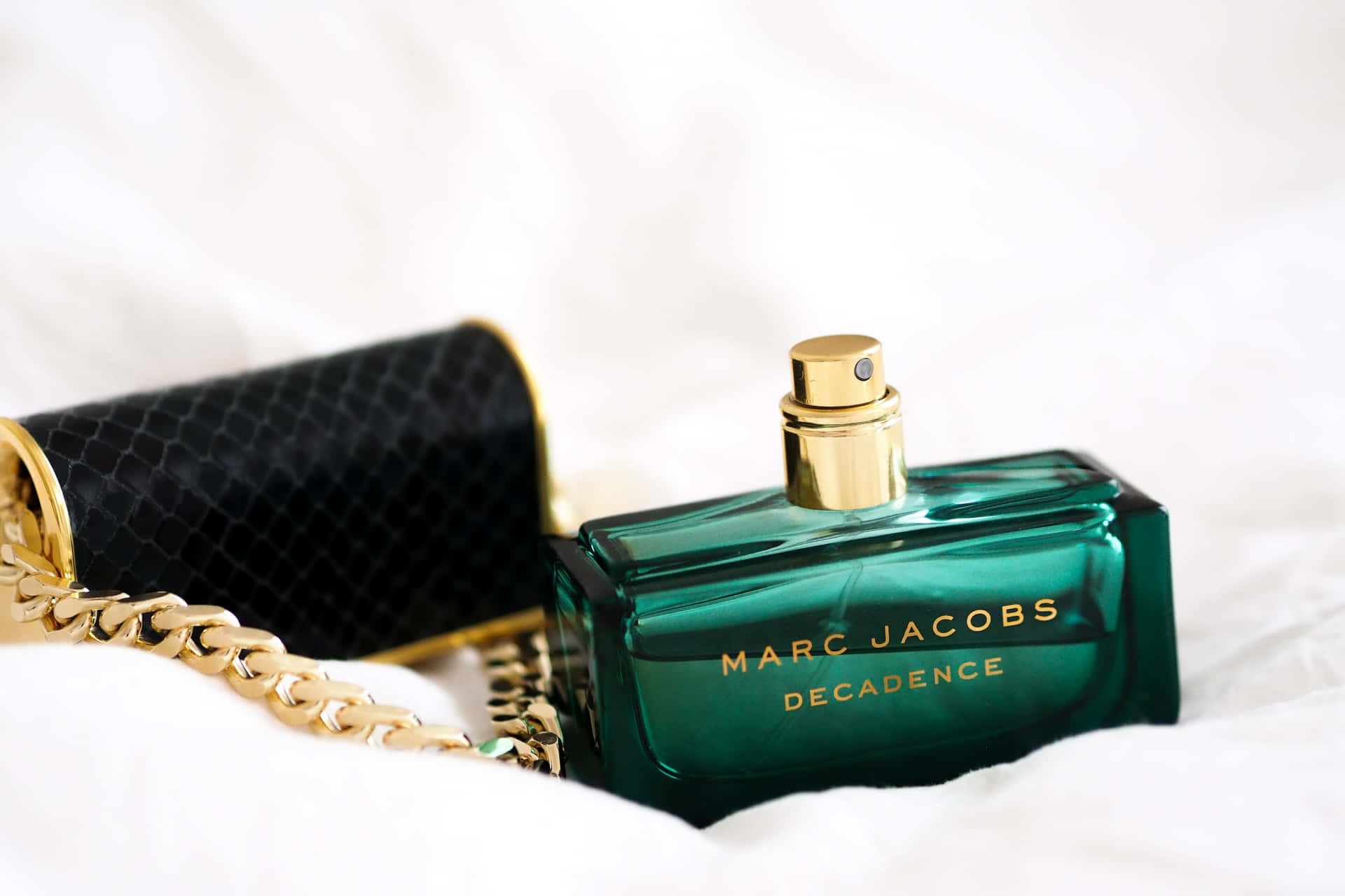 白色布料上的綠色Marc Jacobs Decadence香水瓶和黑色手拿包。