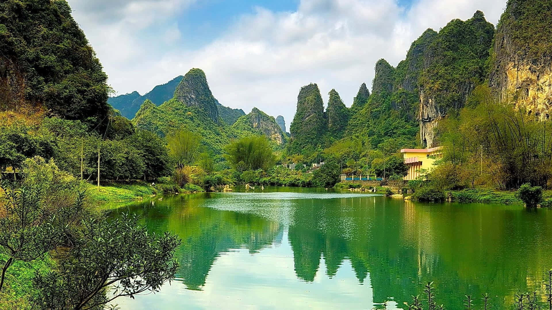 一個寧靜的湖泊，周圍環繞著高聳的綠色山脈，附近有一座小建築。