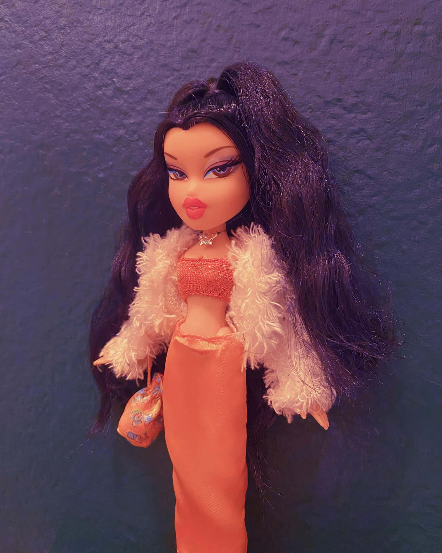 Bratz 公仔穿著帶毛茸茸領子的桃色服裝，拿著小包包，背景是紫色牆壁
