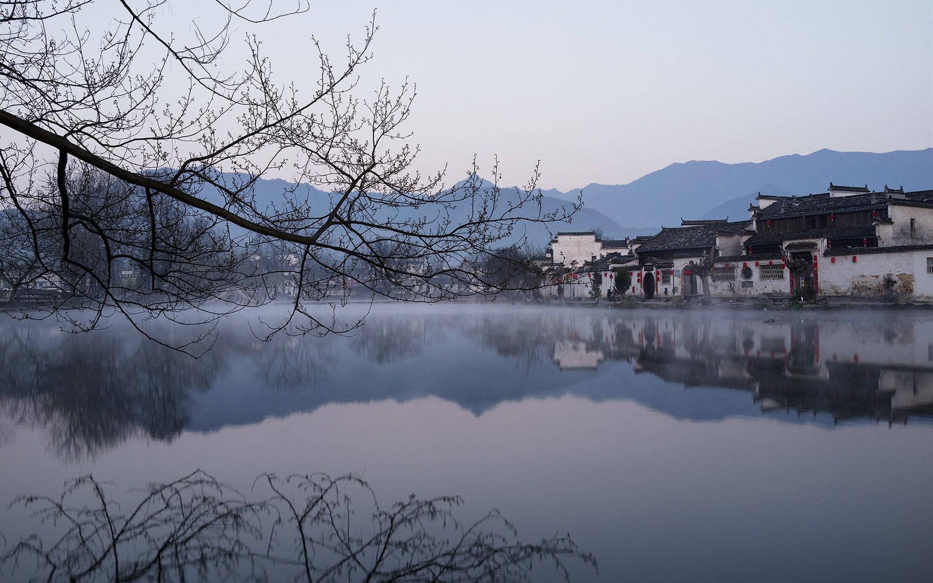 寧靜的霧氣黎明，傳統中國村莊的水中倒影和光禿的樹枝。