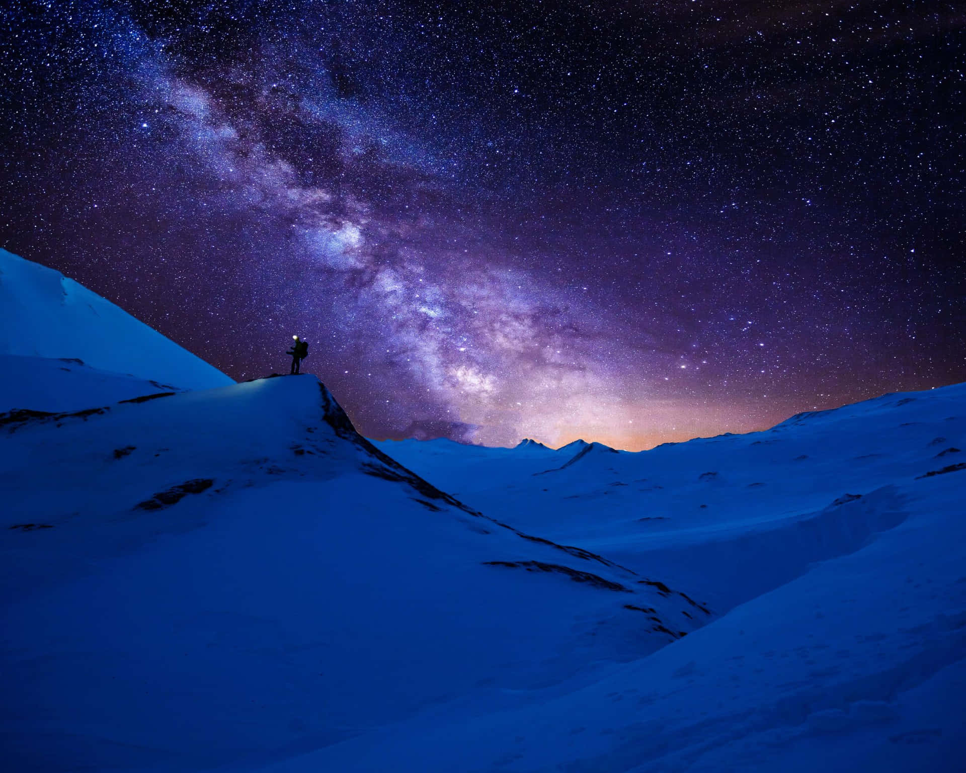 一個人站在白雪覆蓋的山頂上，在燦爛的星空下，銀河閃耀。
