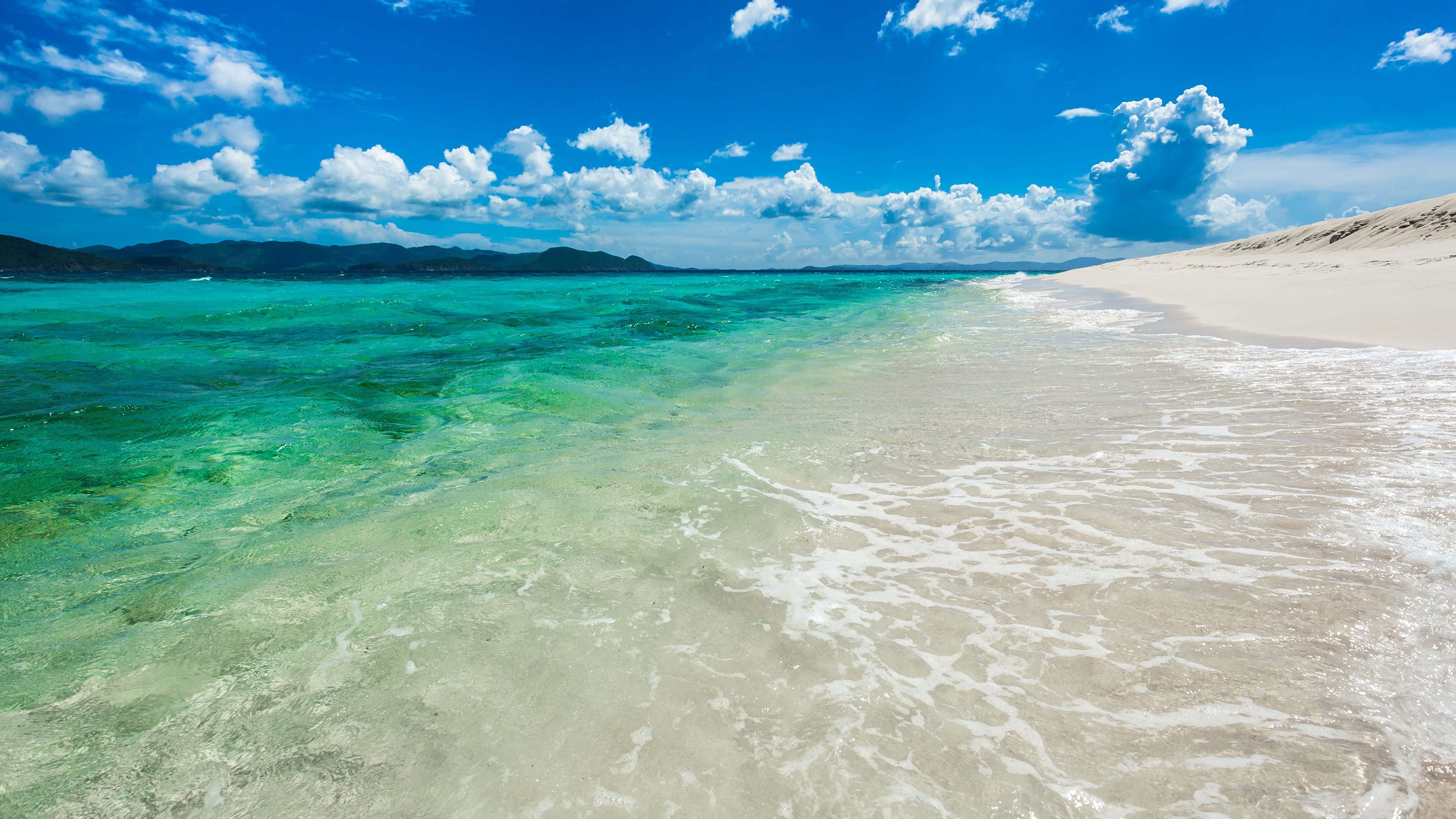 Beach Photography 桌布 壁紙 — 清澈的碧綠海水拍打著純淨的白色沙灘，上方是藍天白雲。
