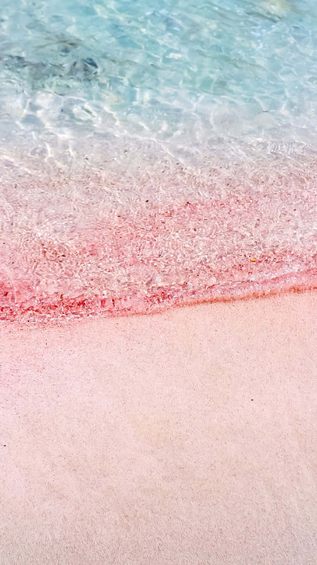 Pink Beach 桌布 壁紙 — 清澈的碧綠海水輕拍柔軟的粉紅色沙灘，呈現寧靜的熱帶海灘景象。