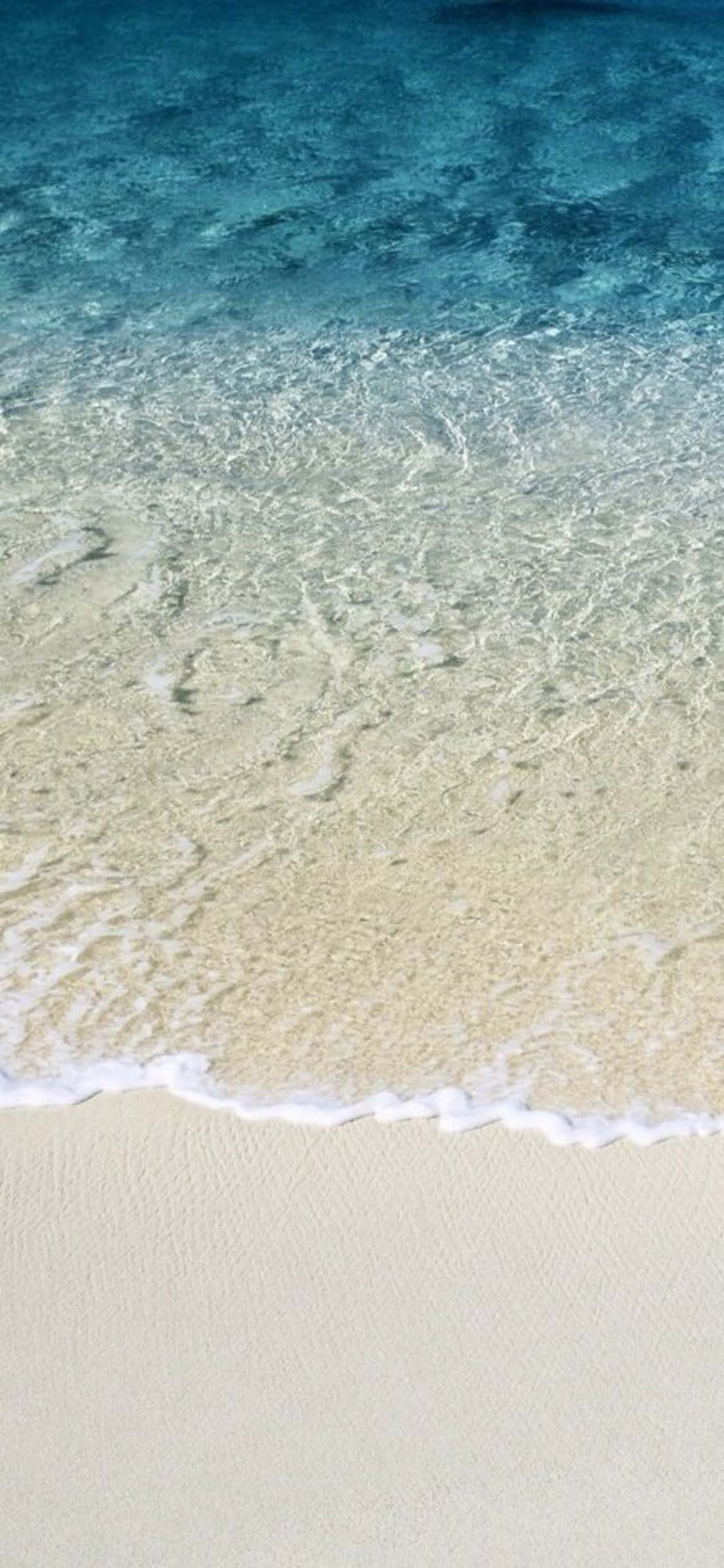 iPhone X Beach 桌布 壁紙 — 清澈的碧綠海浪輕輕拍打純淨的白色沙灘，呈現寧靜的熱帶海灘景象。