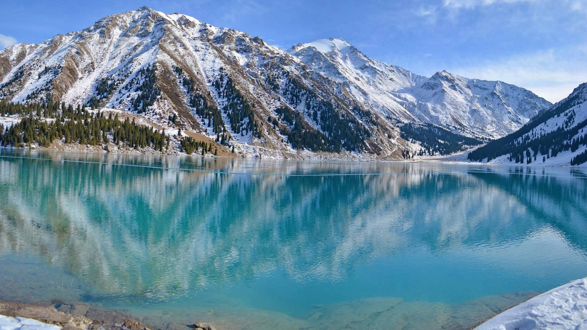 清澈的阿爾馬蒂大湖 壁紙 — 白雪覆蓋的山峰在清澈碧藍的湖水中完美倒映，天空湛藍無雲。
