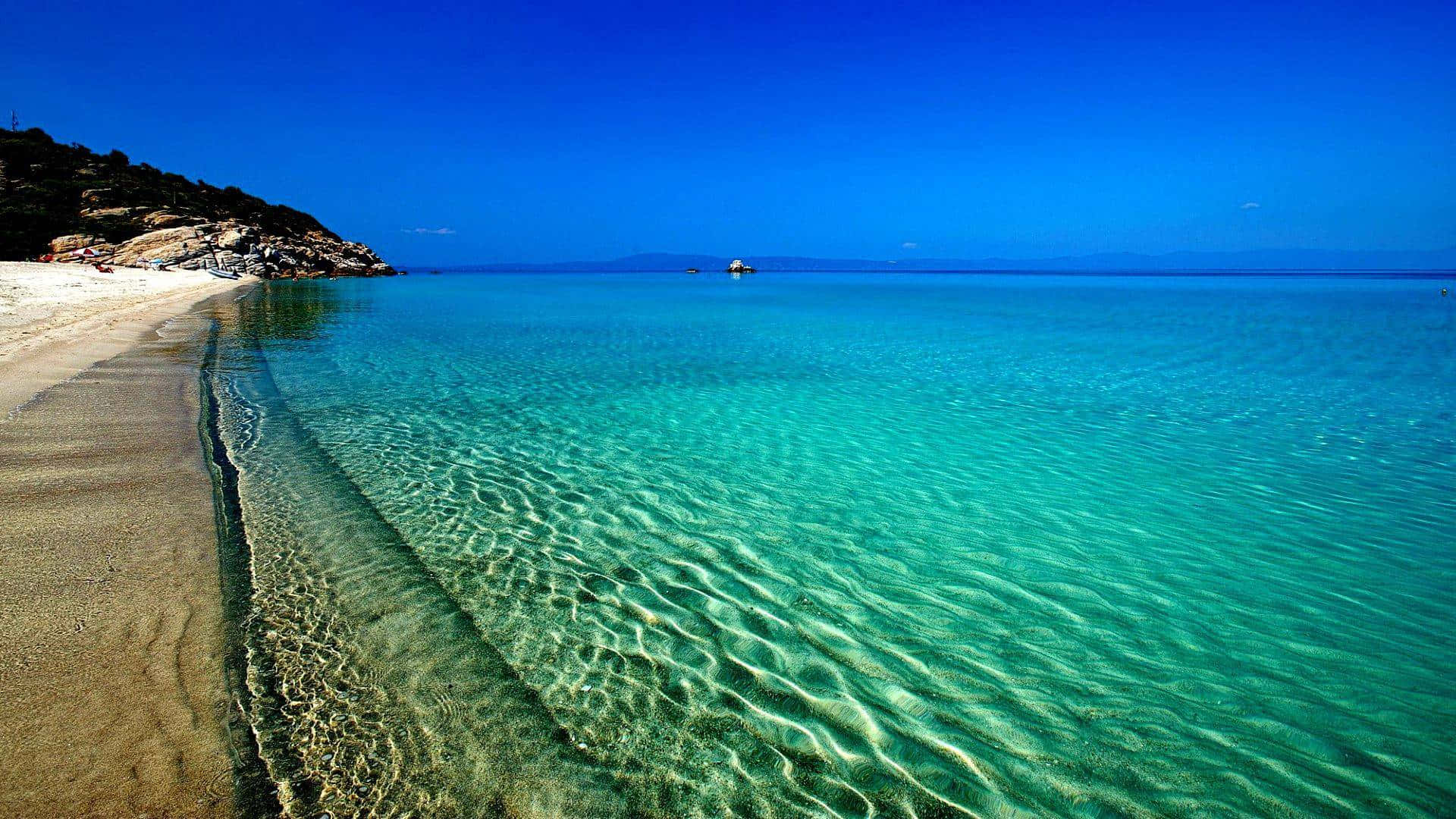 Seashore 桌布 壁紙 — 清澈碧綠的海水在陽光明媚的沙灘上輕輕蕩漾，映襯著充滿活力的藍天。