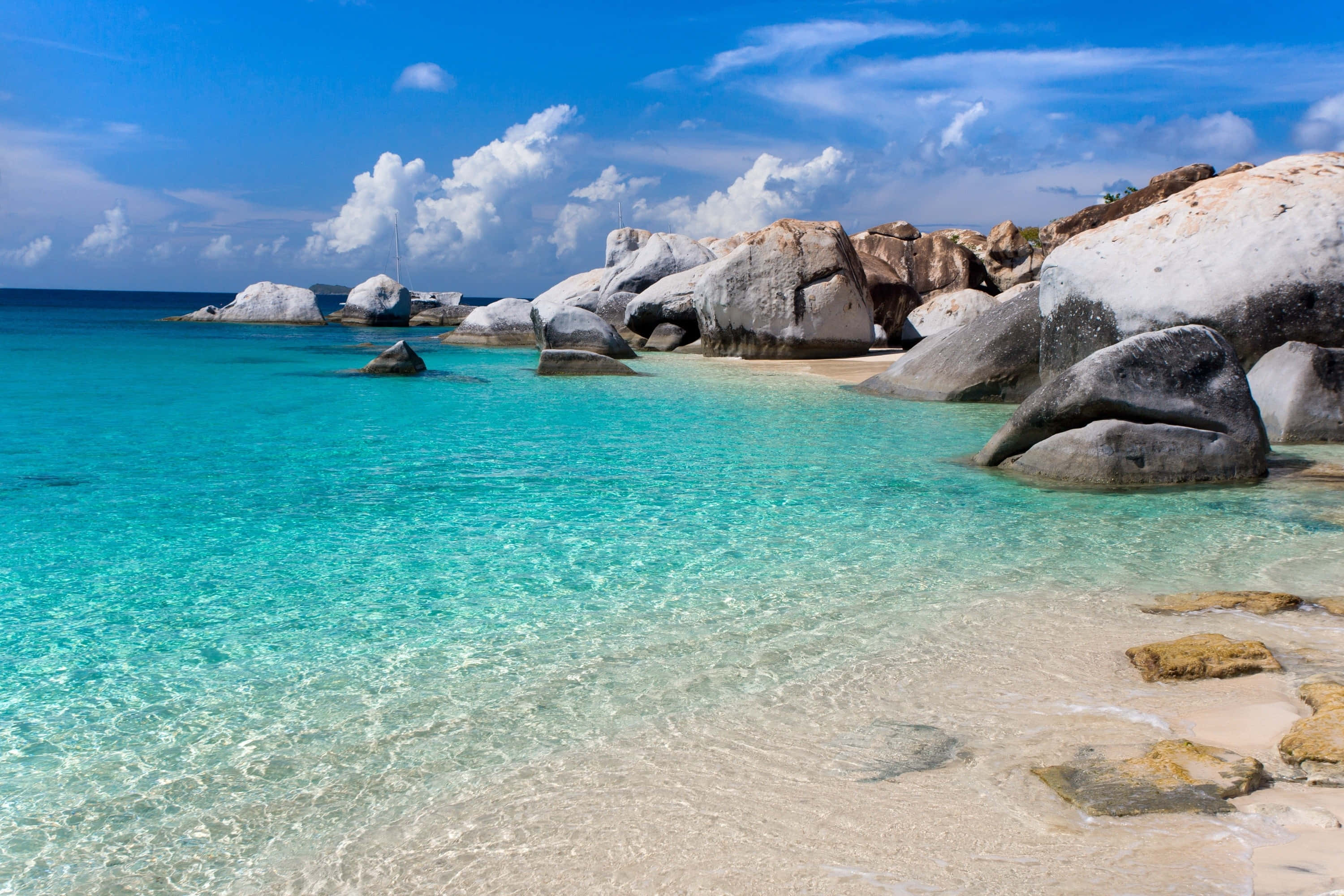 Seychelles Beach 桌布 壁紙 — 清澈碧綠的海水拍打著沙灘，沙灘上散佈著巨大的光滑岩石，頭頂是明亮的藍天和蓬鬆的白雲。
