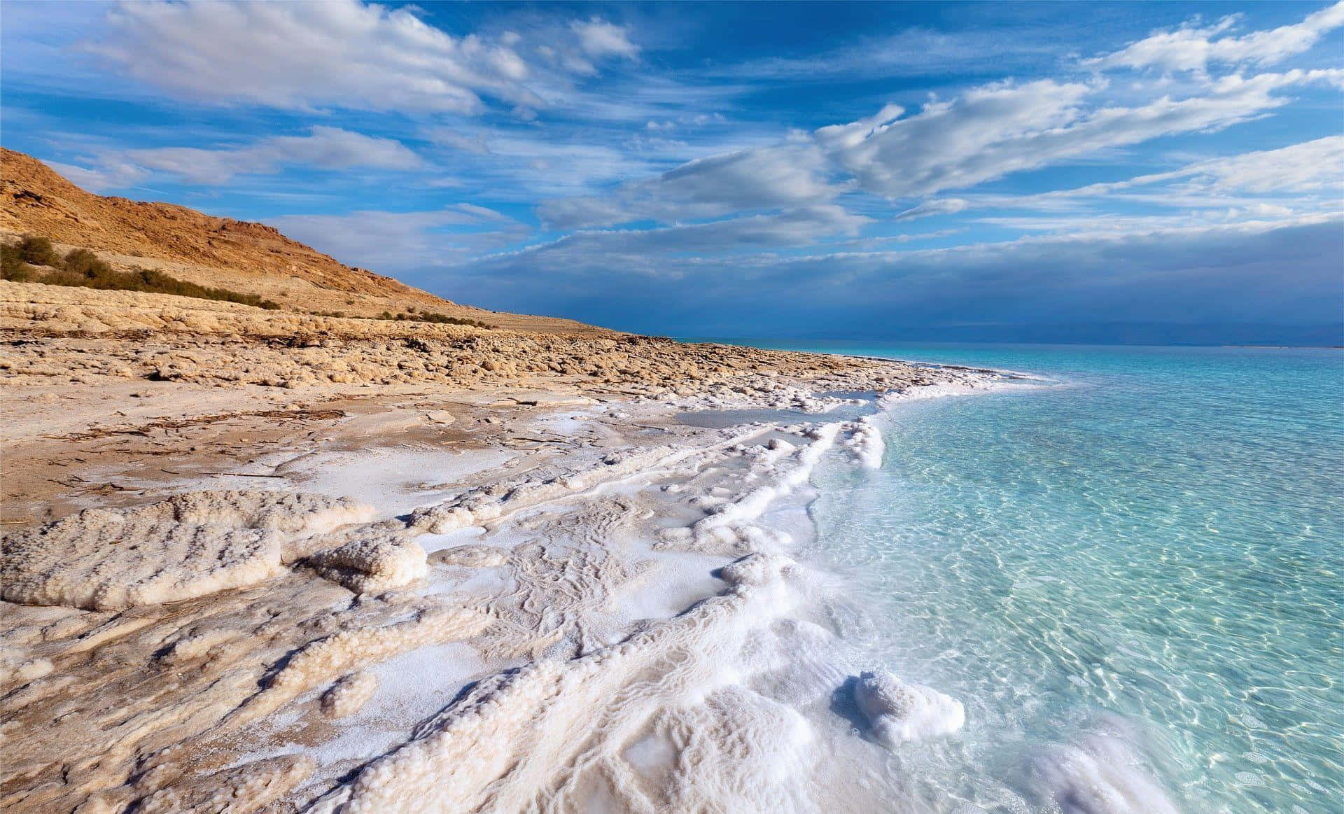 Israel 桌布 壁紙 — 清澈碧綠的海水拍打著由白色鹽結晶形成的崎嶇海岸線，天空湛藍，雲朵點綴其間。