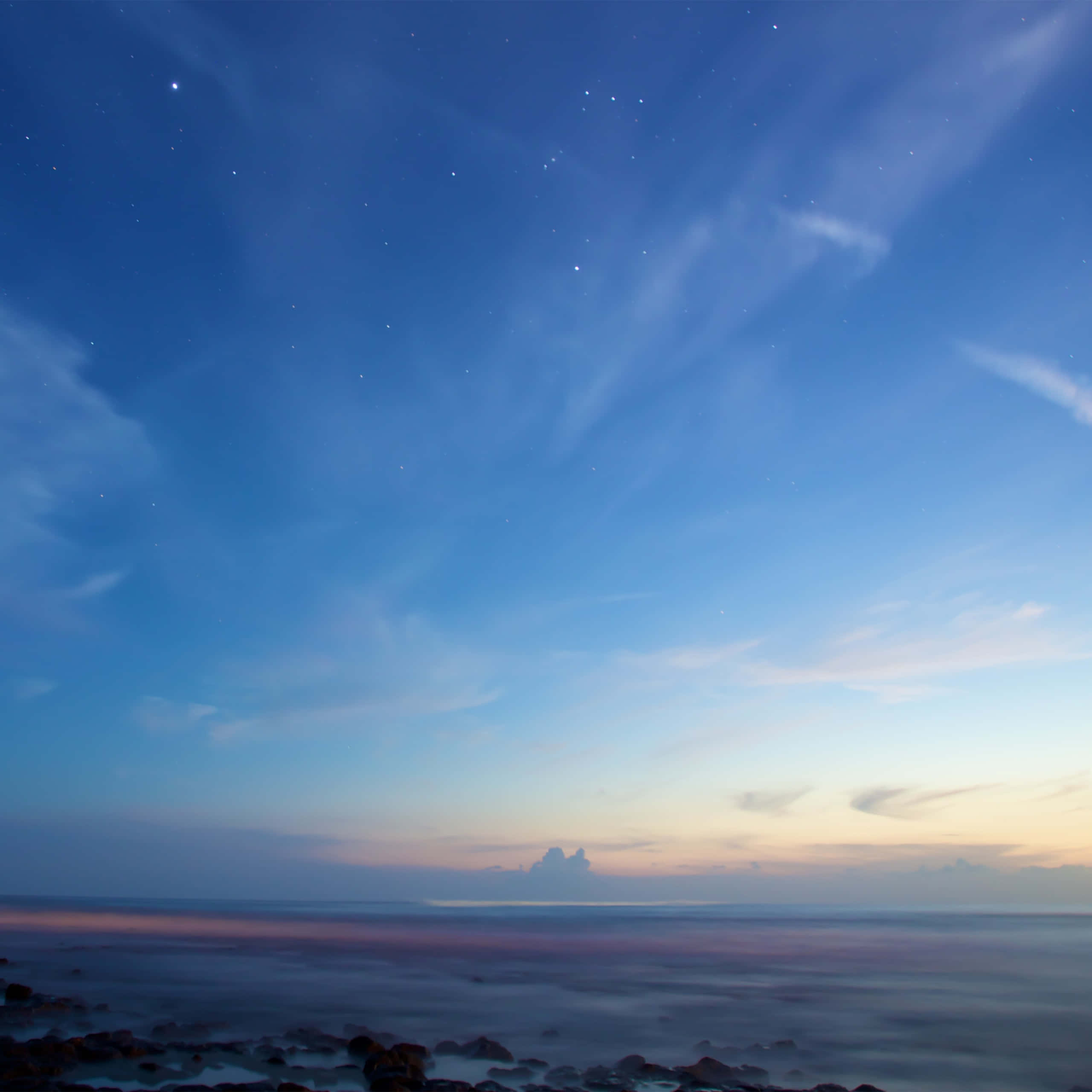 清澈藍色天空的壯麗景色 壁紙 — 寧靜的黃昏海景，星星在溫柔的海浪和剪影岩石上方浮現。