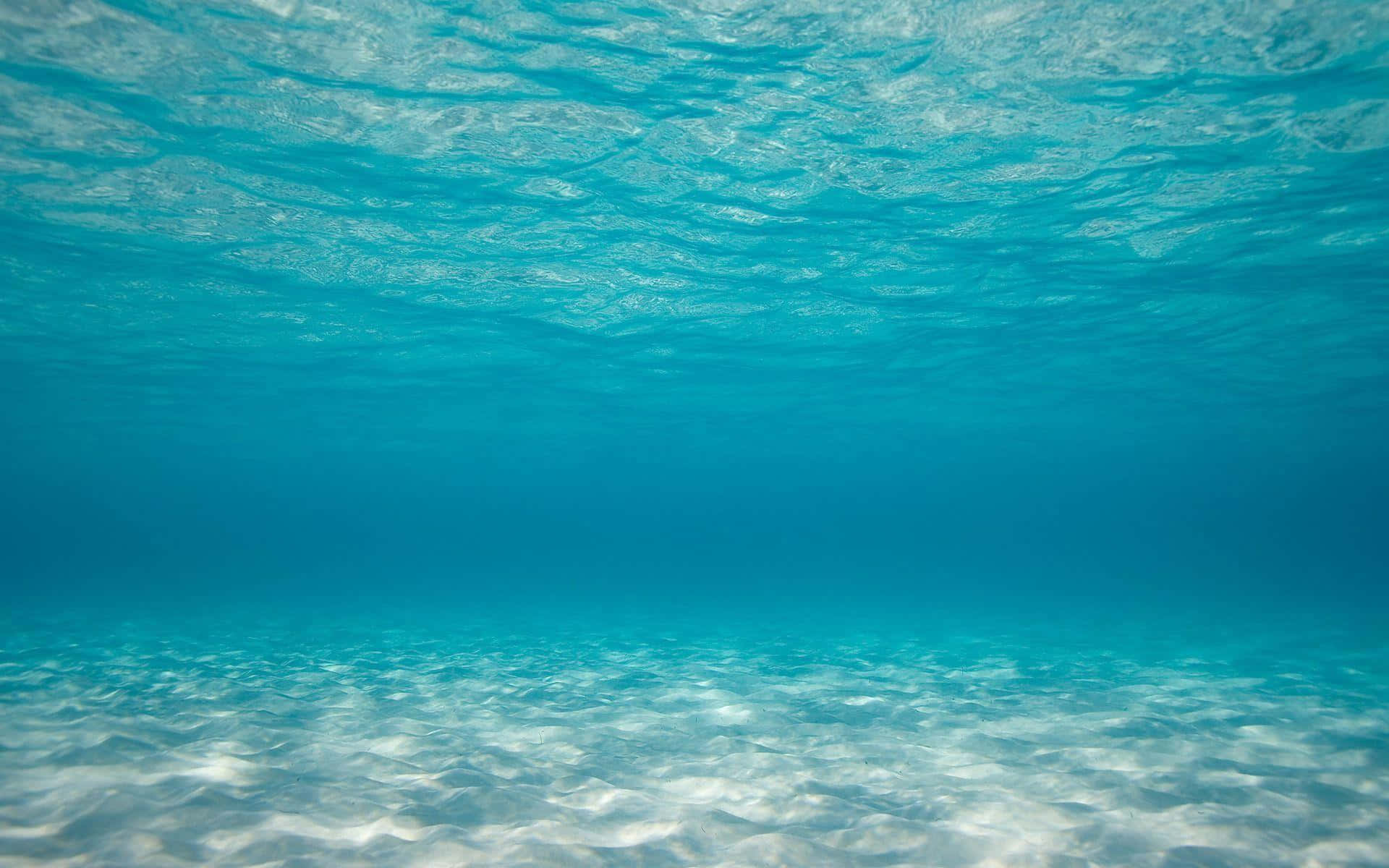 清澈藍色海底圖 壁紙 — 陽光穿過清澈的碧綠海水，照亮了沙質海底，上方有輕柔的漣漪。