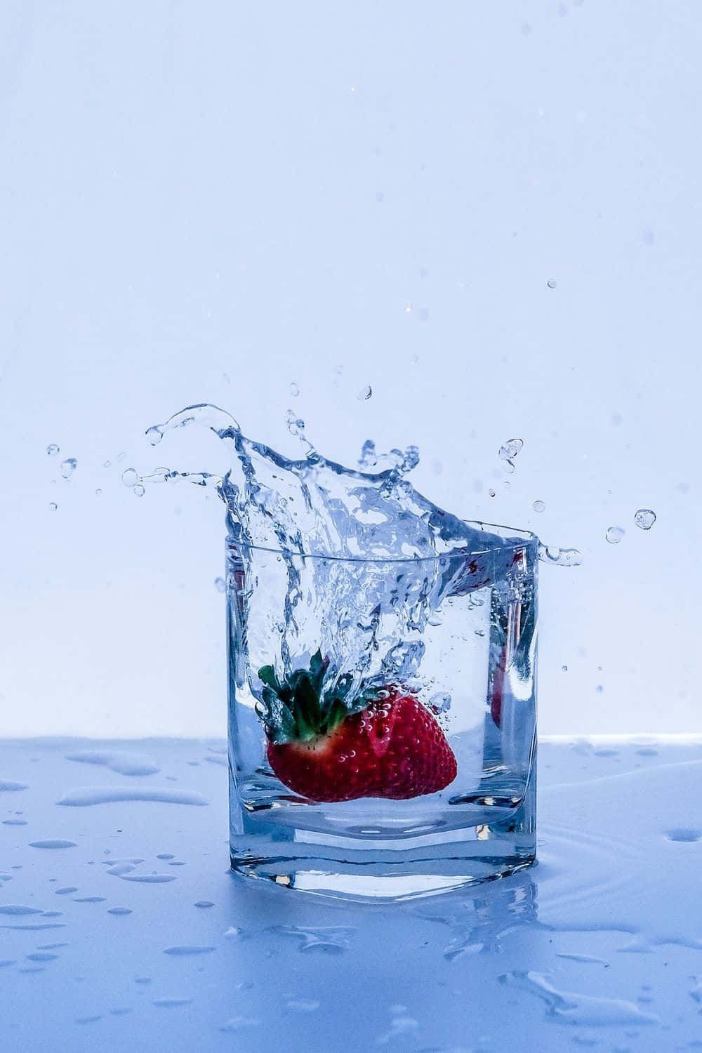 草莓掉進水中，在杯子裡引起水花。