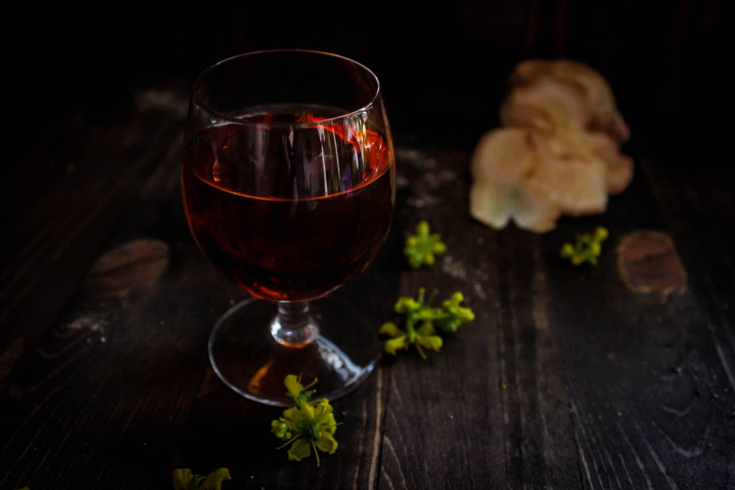 清爽深紅色果味飲料 壁紙 — 一杯濃郁的紅酒在深色木桌上溫暖地發光，旁邊散落著黃色花朵和薯片。