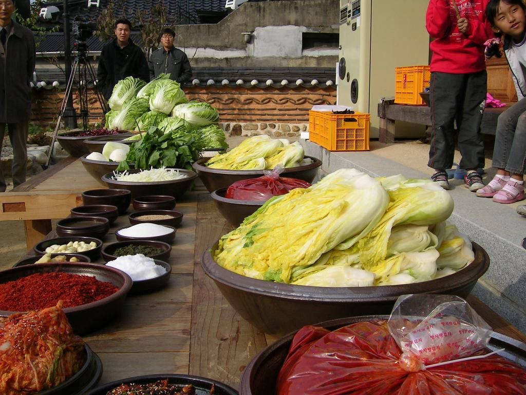 新鮮大白菜和泡菜配料在戶外木桌上展示。