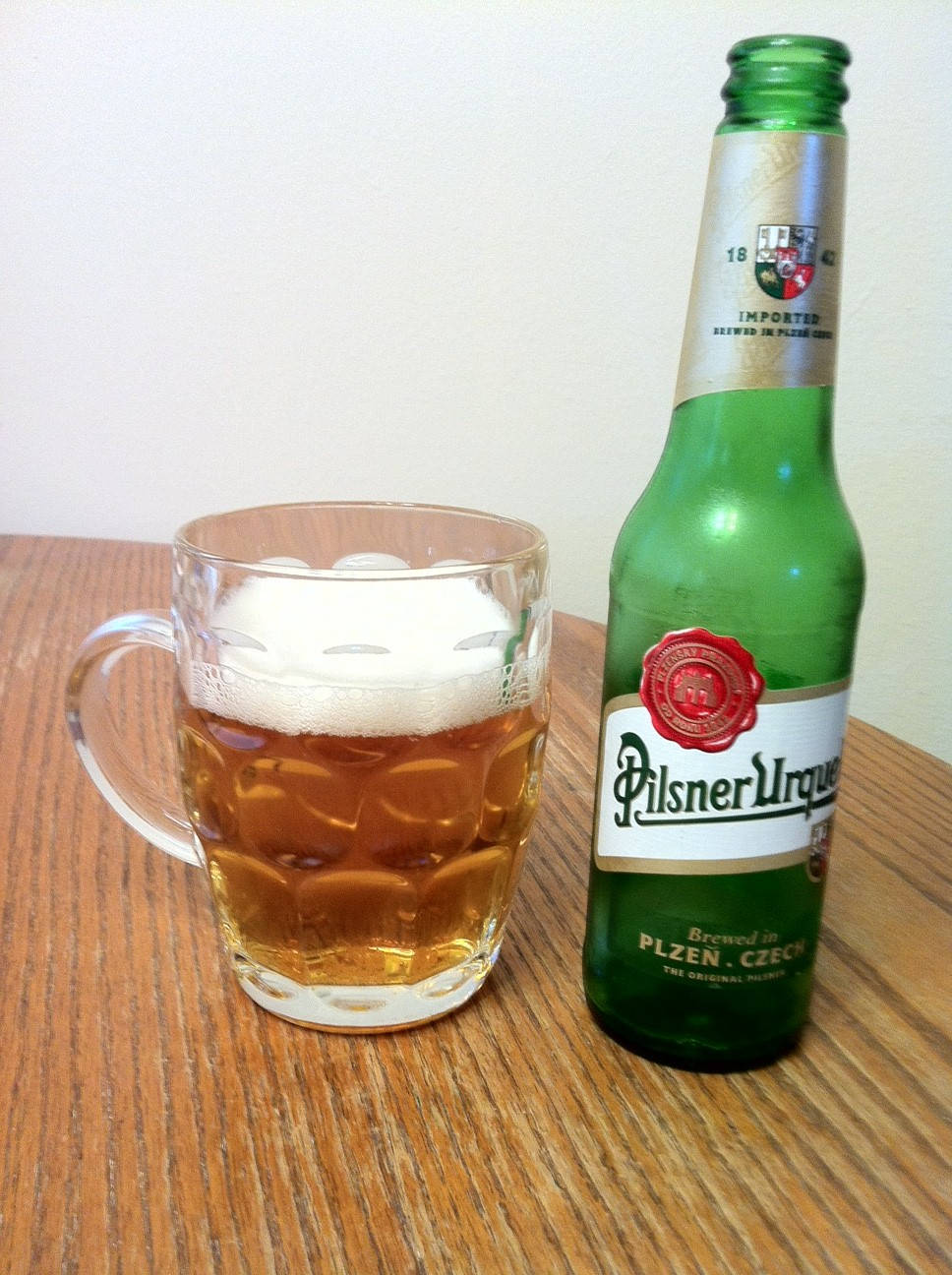 一個綠色Pilsner Urquell啤酒瓶和一個玻璃啤酒杯放在木桌上。