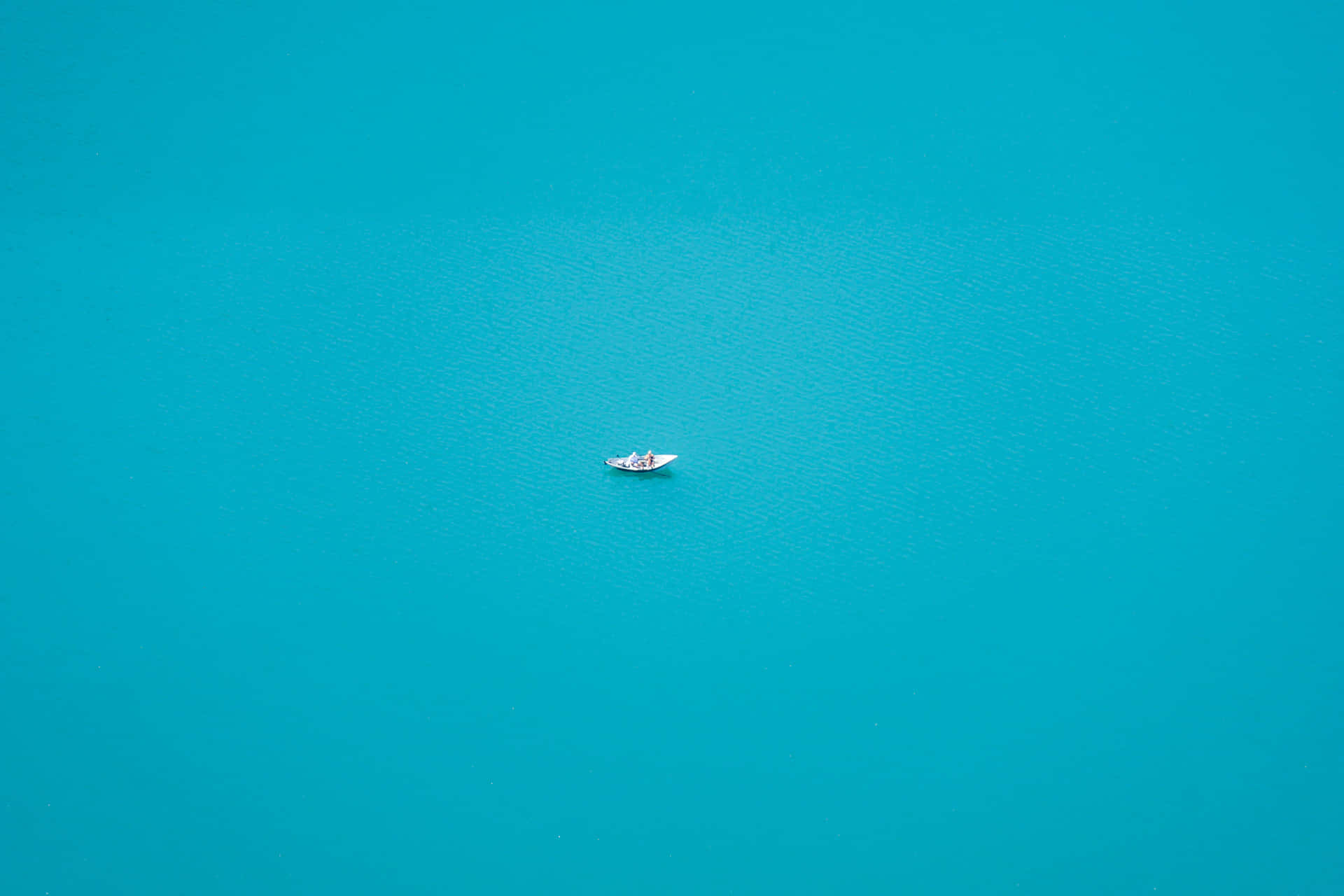 從高空俯瞰，一艘小小的白色皮划艇獨自漂浮在平靜的碧綠水面上。