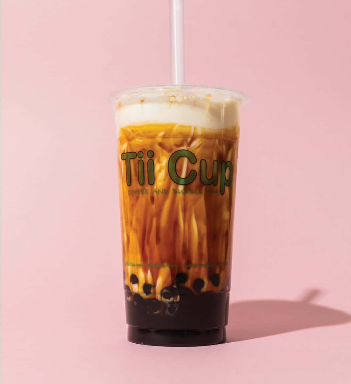 清爽美味的珍珠奶茶 壁紙 — 一杯高身凍咖啡泡泡茶，帶有奶油泡沫和黑珍珠，放在品牌杯中，背景是柔和的粉紅色。