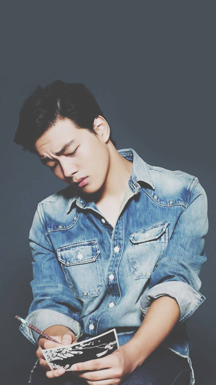 清爽造型 Yeo Jin Goo 壁紙 — 一位穿著牛仔襯衫的年輕男子身體前傾，專注地用鉛筆在一張小卡片上素描黑白花卉圖案。