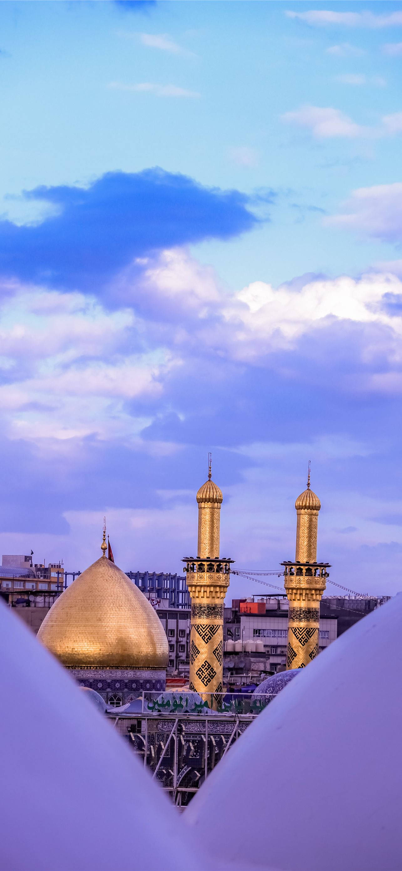Karbala 桌布 壁紙 — 清真寺的金色圓頂和宣禮塔在暮色天空下閃耀，伴隨著柔和的紫色雲彩。