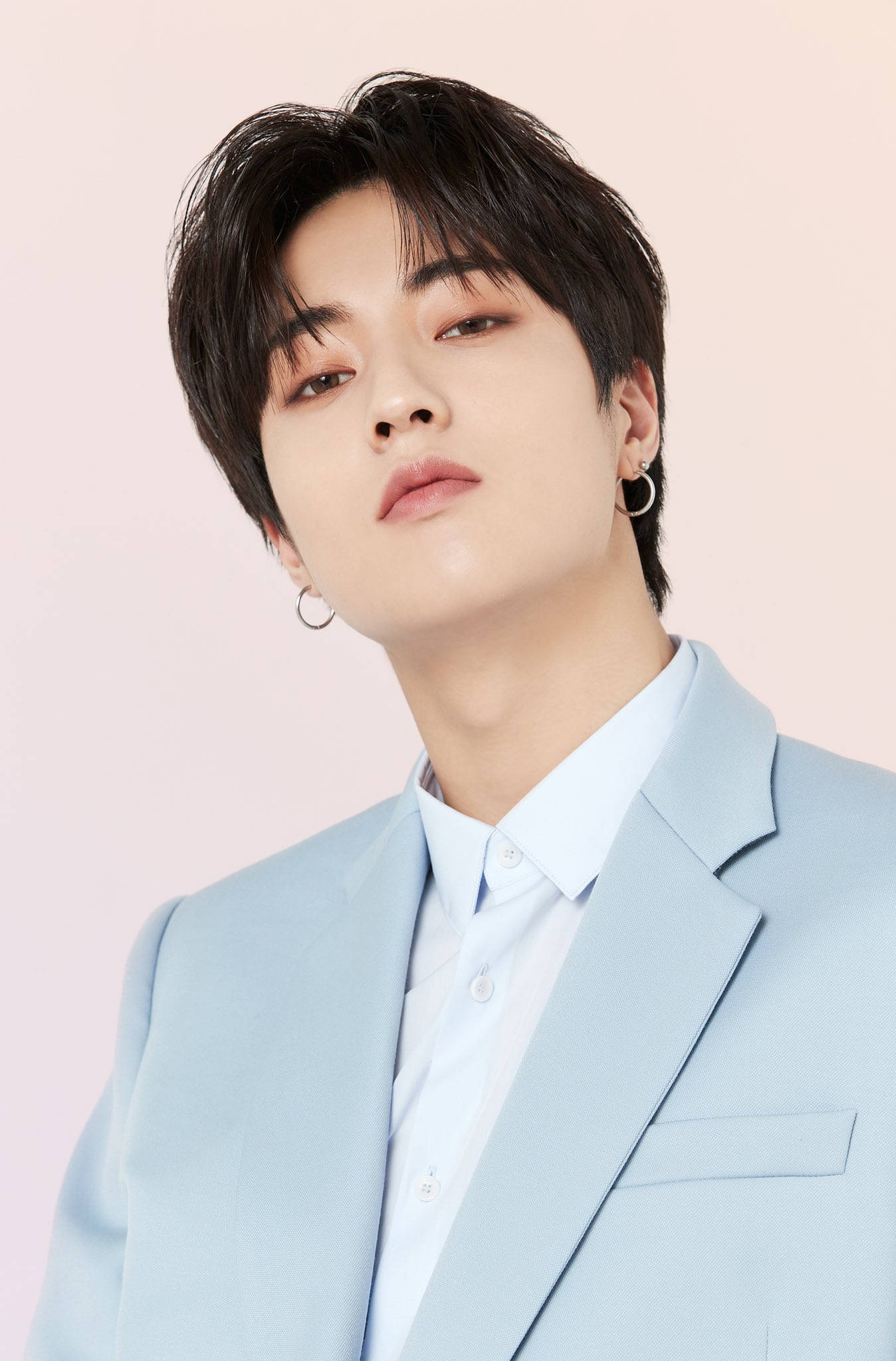 渡邊一馬 K-POP視覺系壁紙 壁紙 — 一位深色頭髮、戴著圈圈耳環的年輕男子，身穿淺藍色西裝，在柔和的粉紅色背景前向上凝視。