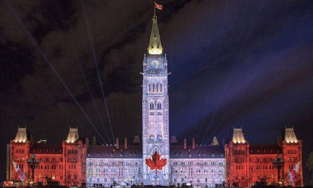 渥太華議會山的極光表演 壁紙 — 加拿大國會大樓在夜間被紅燈照亮，外牆上有巨大的楓葉投影。