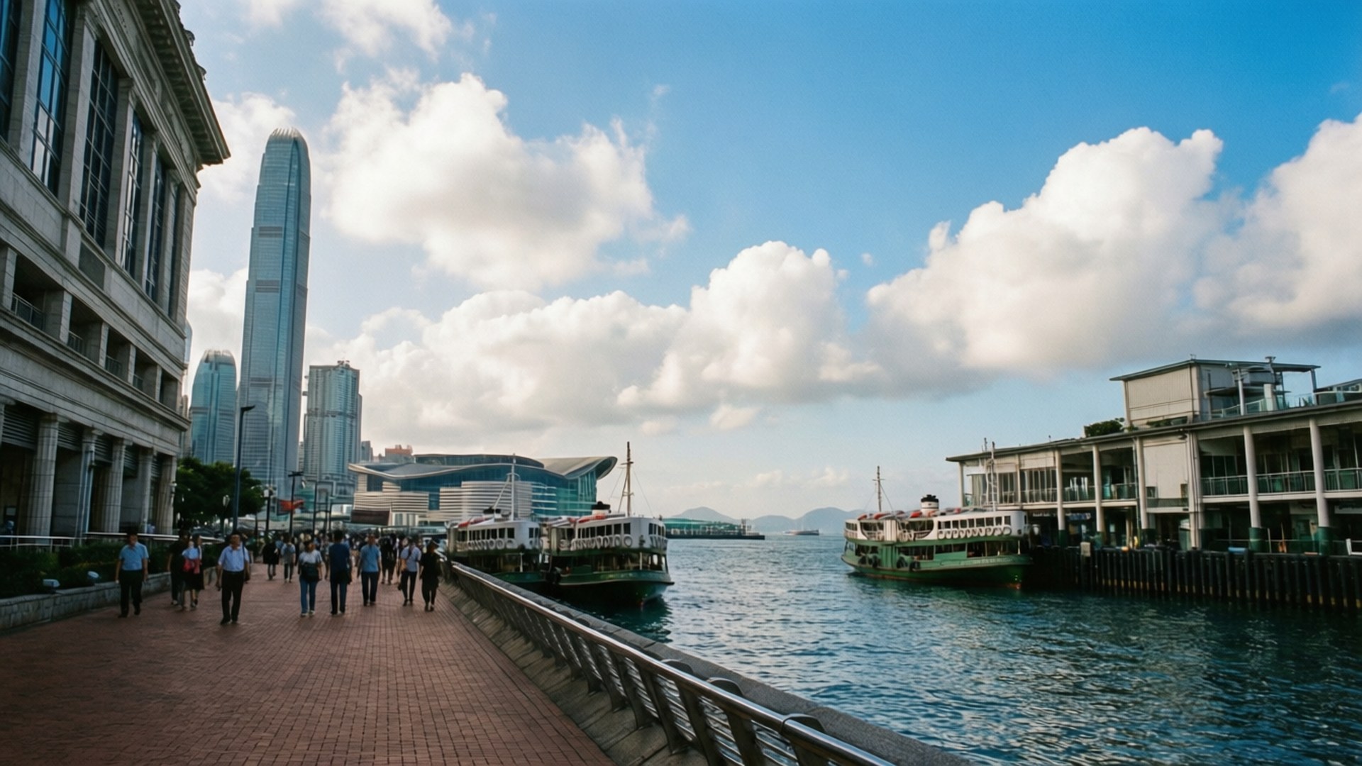 行人沿著海濱長廊行走，背景有渡輪和摩天大樓。
