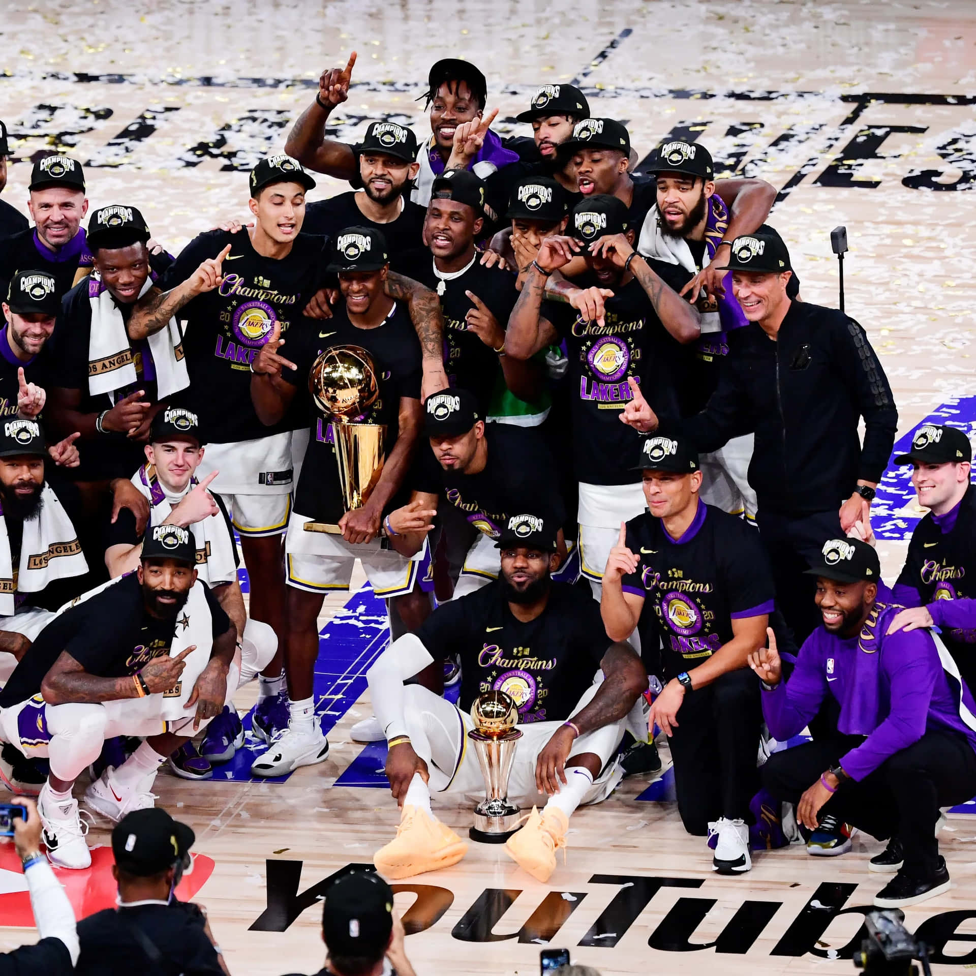 湖人隊2020 NBA冠軍慶祝 壁紙 — 洛杉磯湖人籃球隊在球場上以獎盃、五彩紙屑和歡樂姿勢慶祝冠軍勝利。