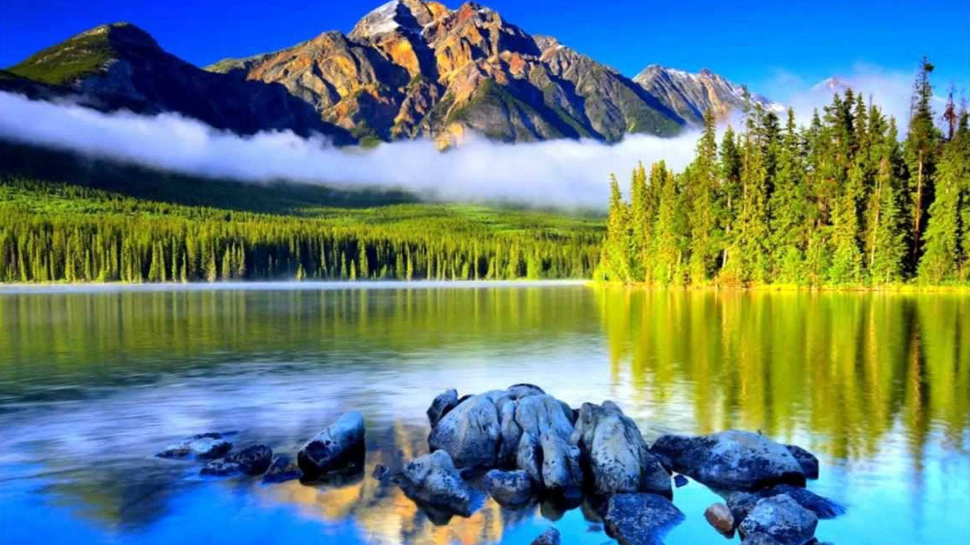 湖光山色森林 壁紙 — 寧靜的山湖在清澈的藍天下倒映著高聳的山峰和茂密的綠色森林。