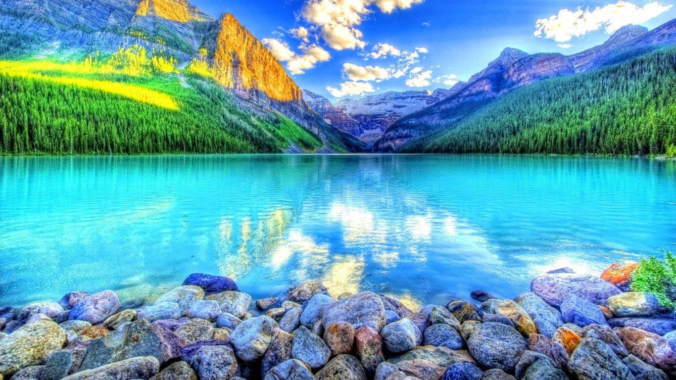 湖景配鮮豔藍色湖水 壁紙 — 一個充滿活力的綠松石湖在明亮的藍天下映照著金色的山脈和蓬鬆的雲朵。