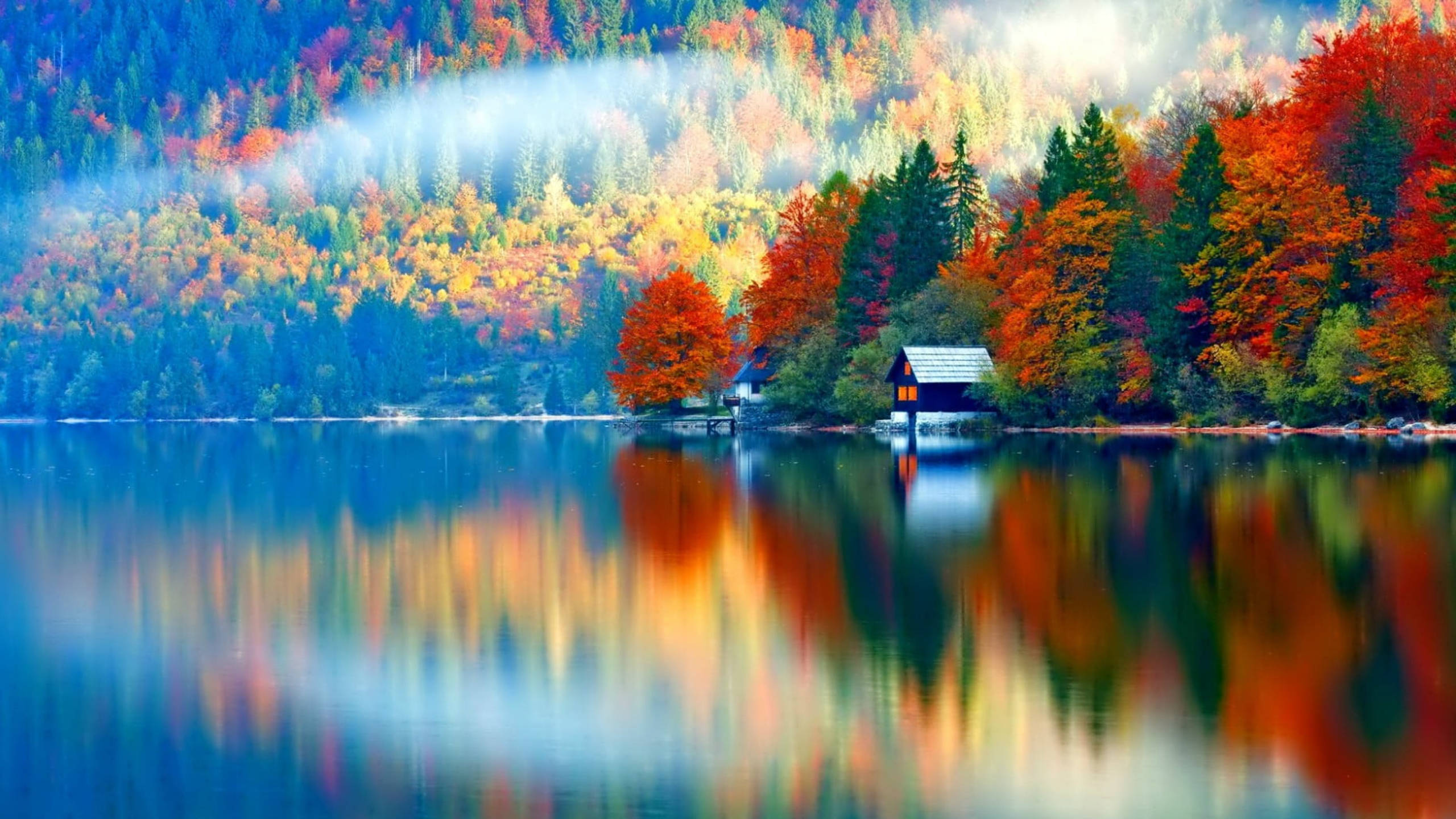 湖畔別墅 Google Meet 虛擬背景 壁紙 — 寧靜的秋日湖泊映照出一片森林，紅、橙、金色的樹葉圍繞著一座孤獨的木屋，宛如燃燒般絢麗。