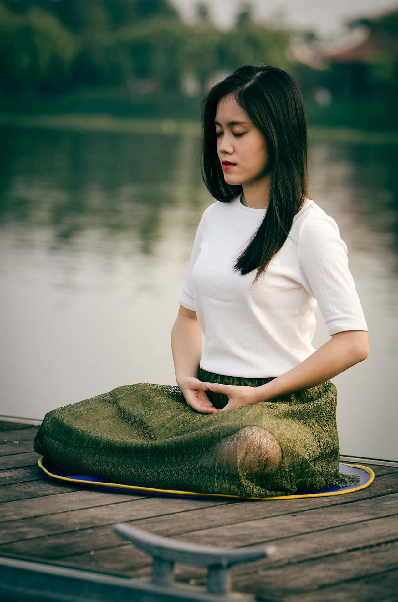 女性在平靜湖邊的木製碼頭上冥想