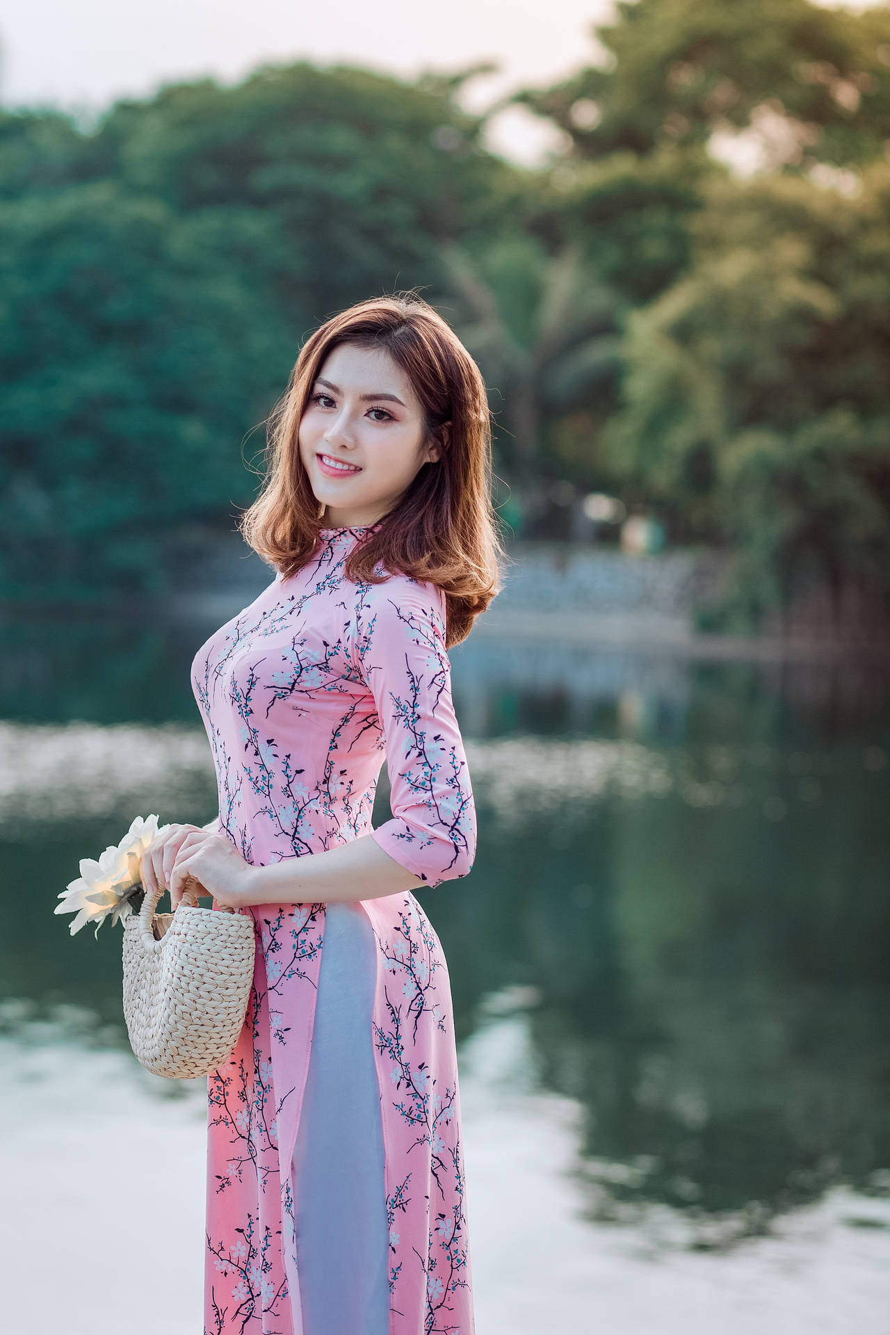 身穿粉紅色奧黛的女性手持竹袋在湖邊
