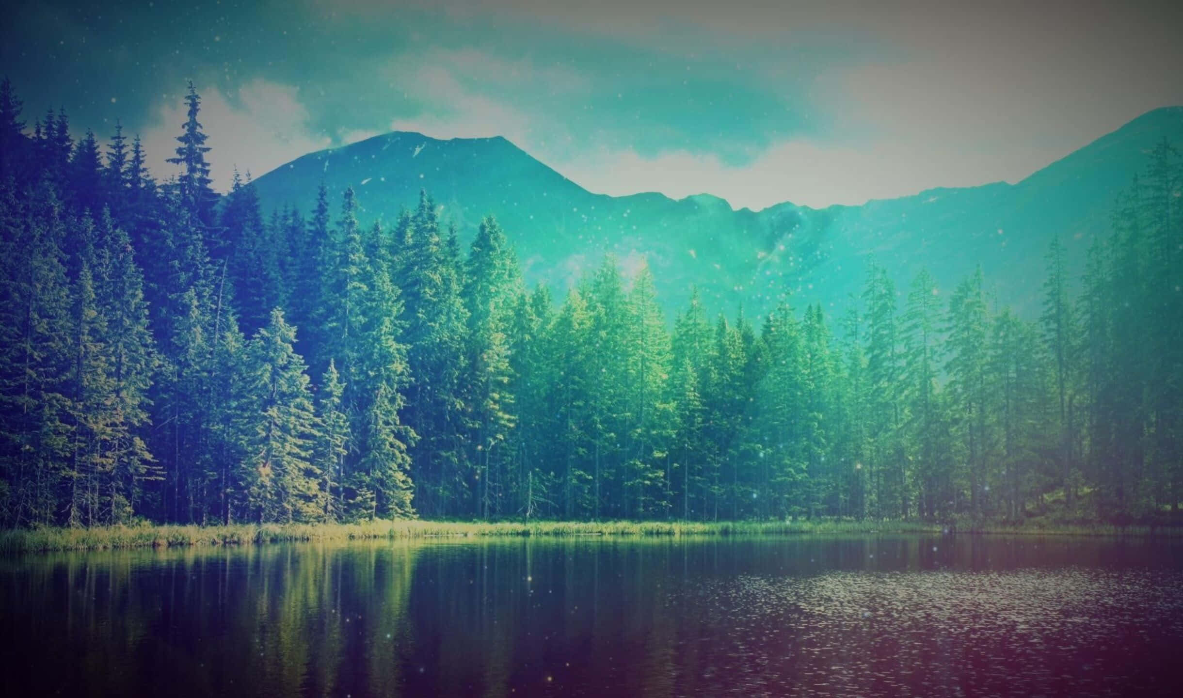 湖畔松林與遠山 壁紙 — 一個寧靜的湖泊映照著茂密的松樹林和霧氣籠罩的山脈，在青綠色的天空下飄著柔軟的雪花。