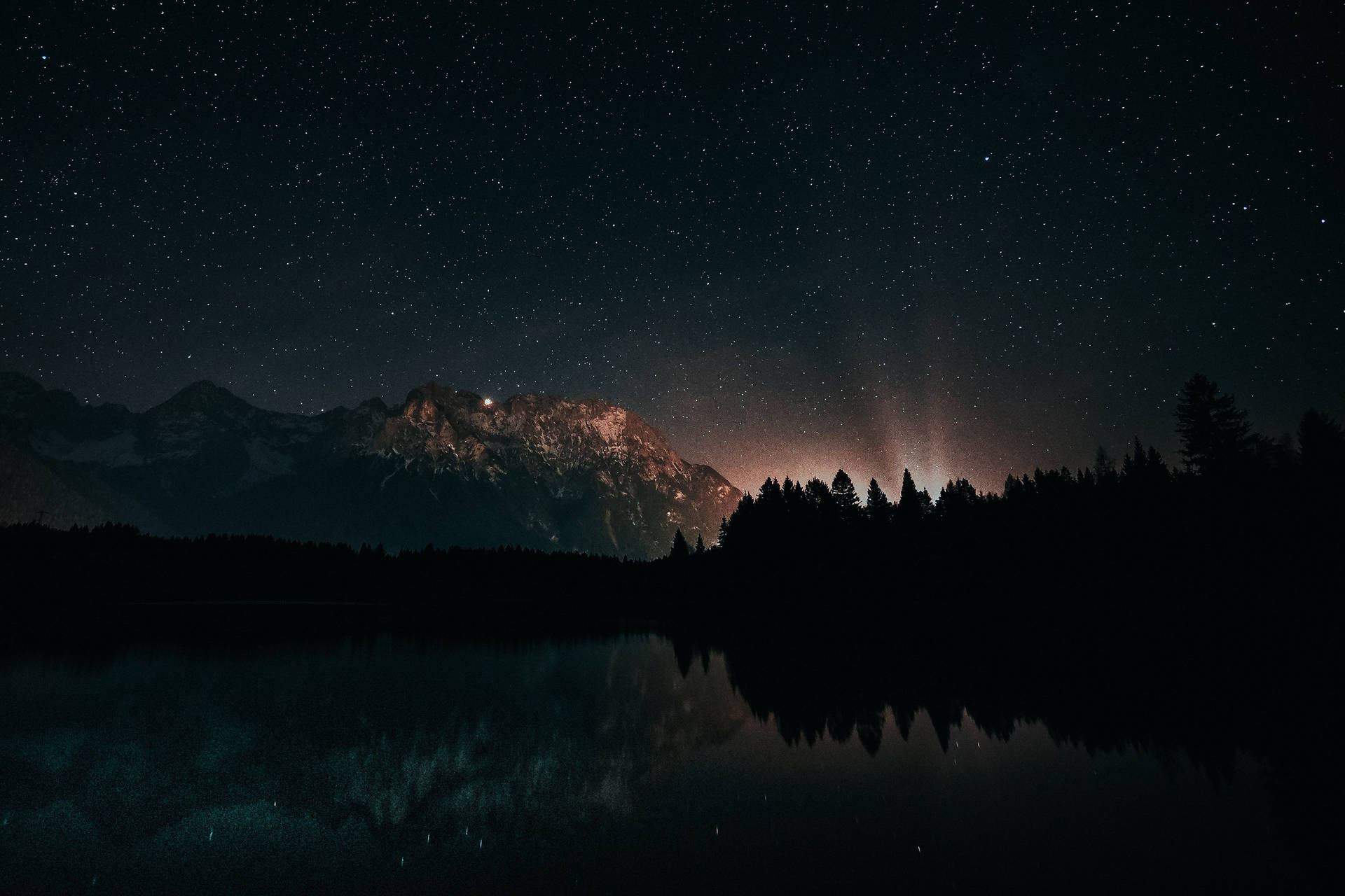 星空夜空與極光映照在被山脈和樹木環繞的湖面上。