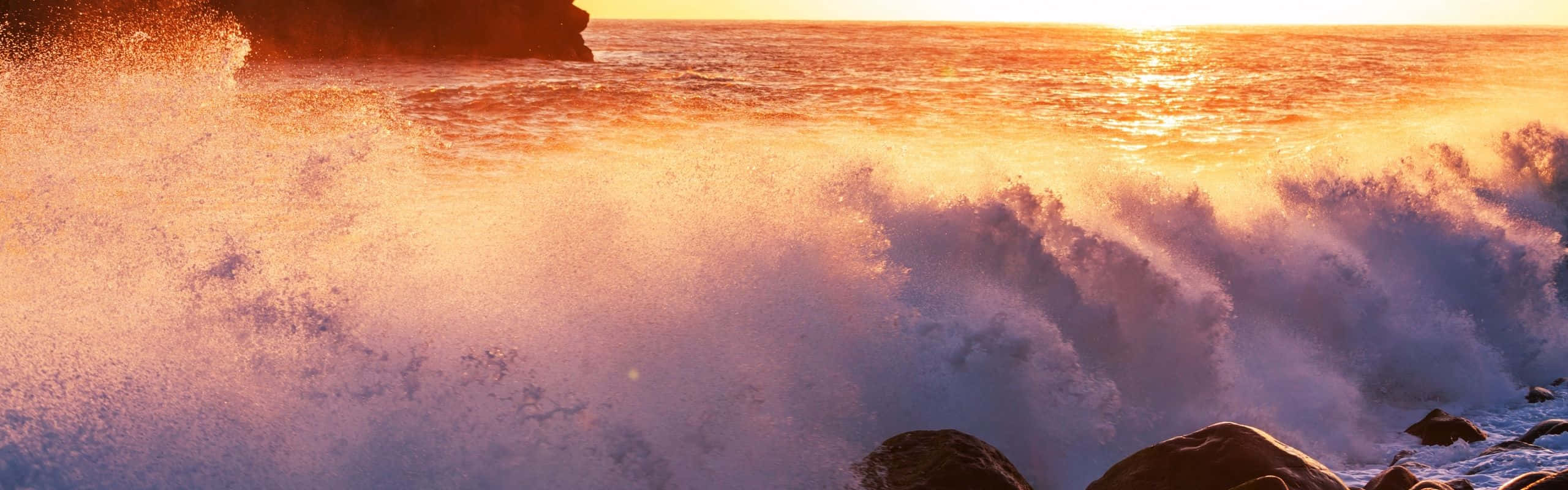 日落時海浪拍打黑暗的岩石，帶有金色和紫色的色調。