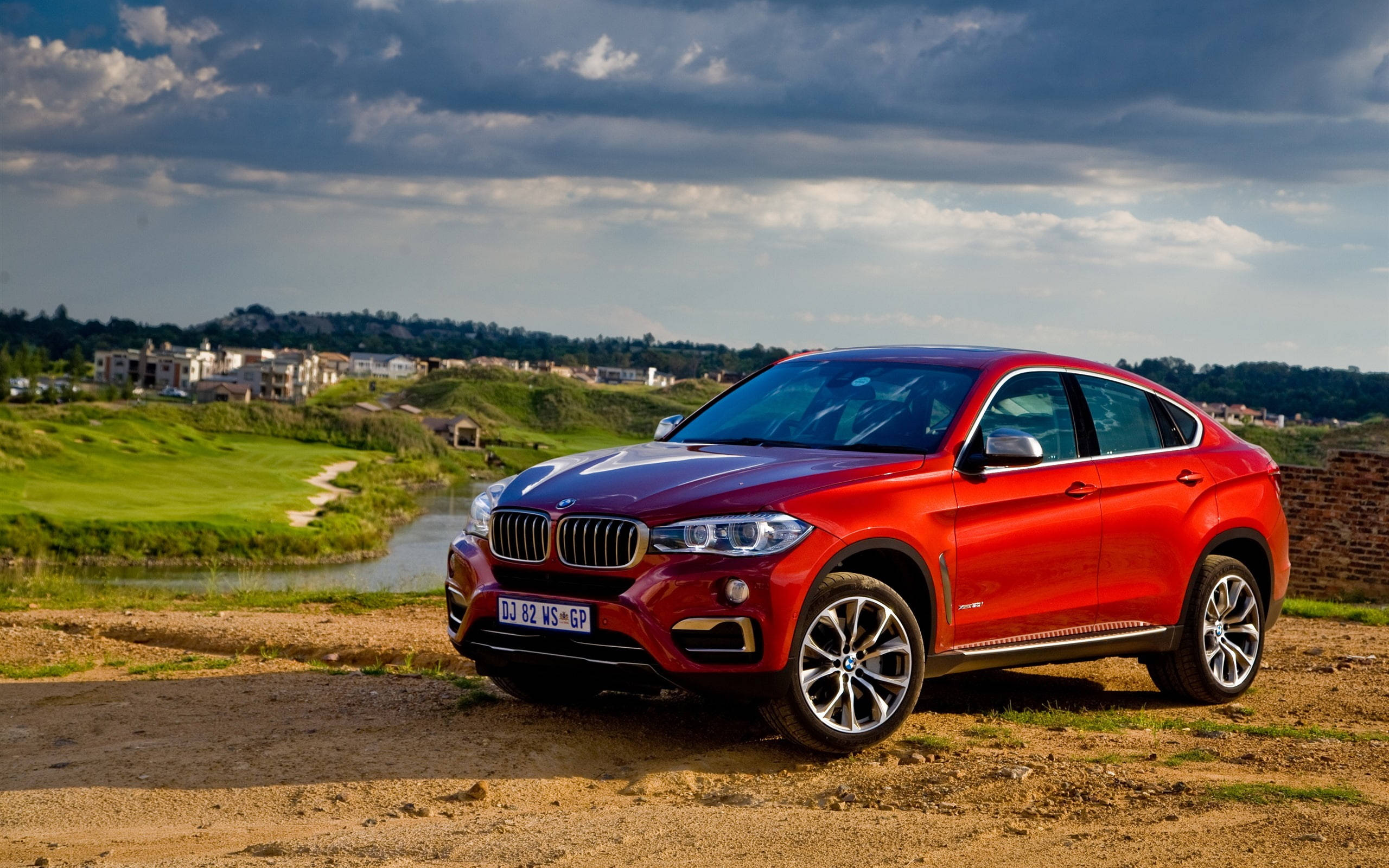 湖畔紅色BMW X6 M跑車 壁紙 — 一輛光澤的紅色BMW X6 SUV停在高爾夫球場旁邊的泥路上，天空多雲，氣氛戲劇化。