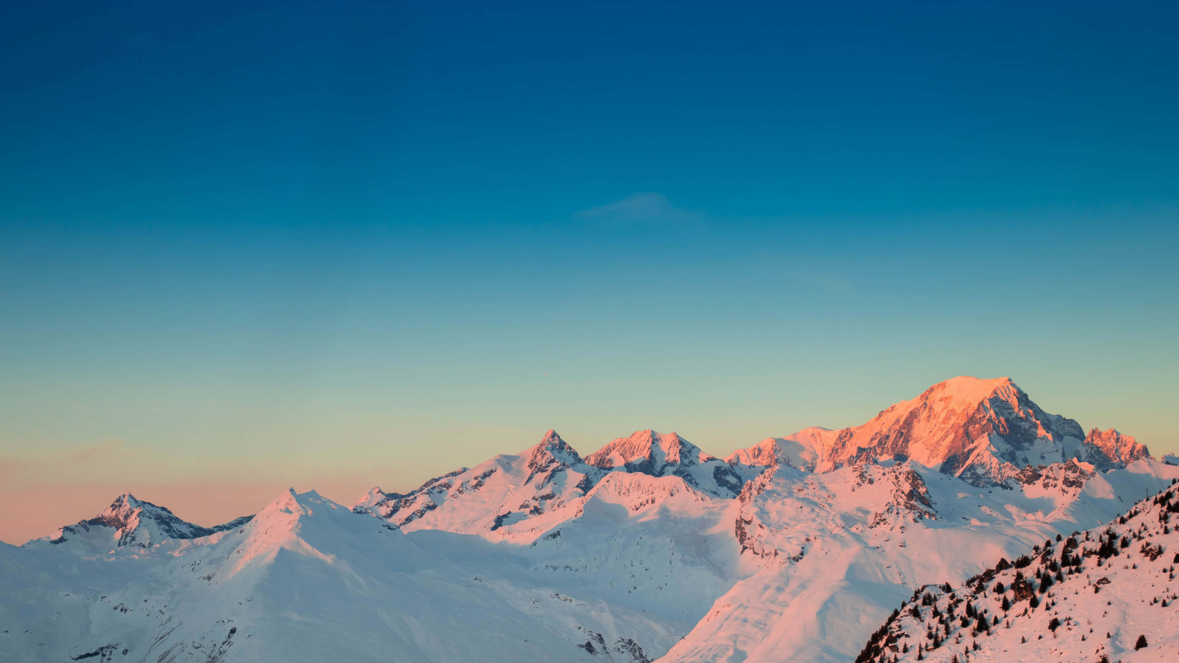 湖畔自然美景 壁紙 — 積雪的山峰在日出時散發著溫暖的粉紅色光芒，映襯著漸變的藍色天空。