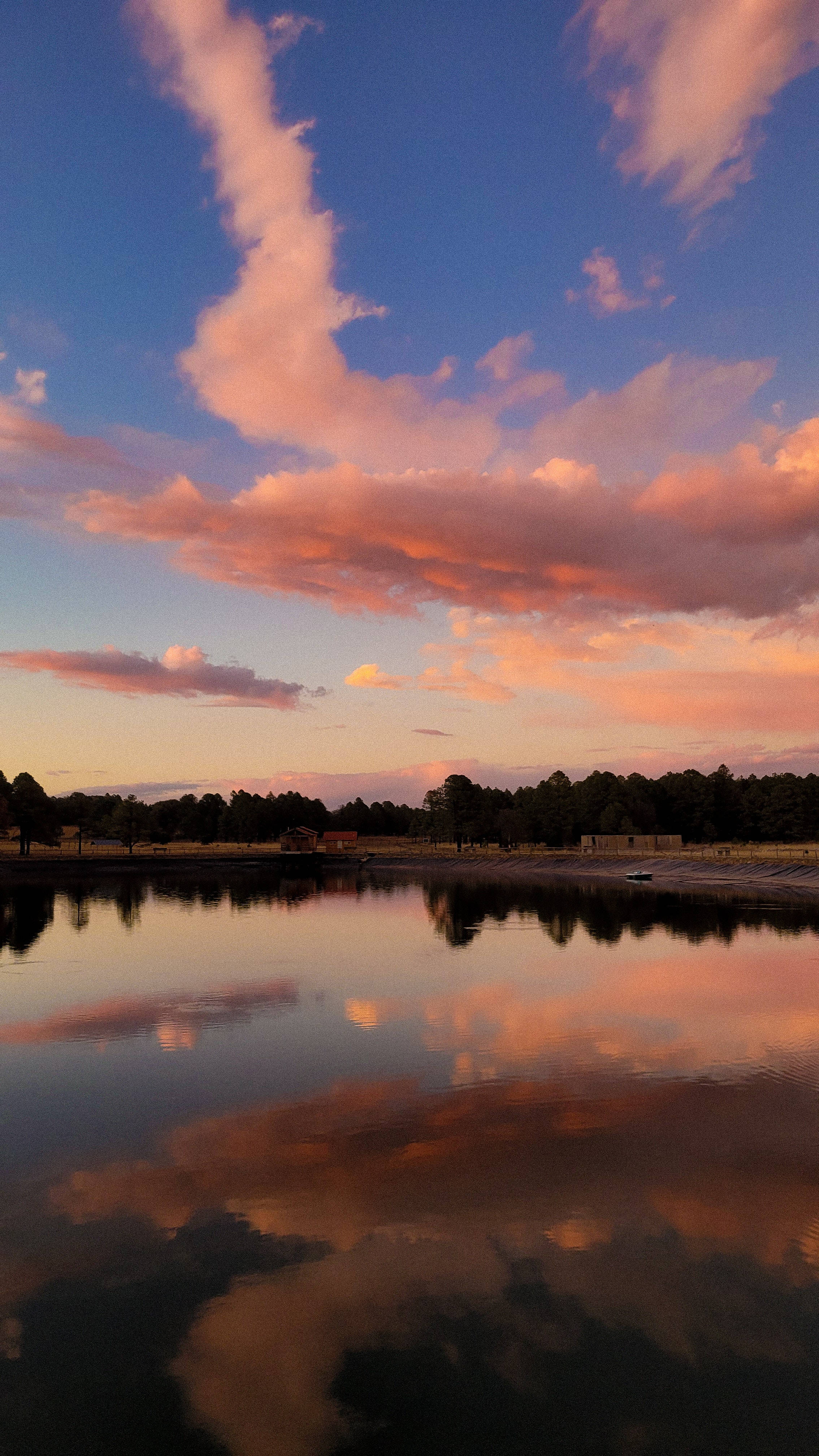 湖畔雲影背景 壁紙 — 寧靜的湖泊映照出深藍色暮色天空中火紅的粉紅色和橙色雲彩。
