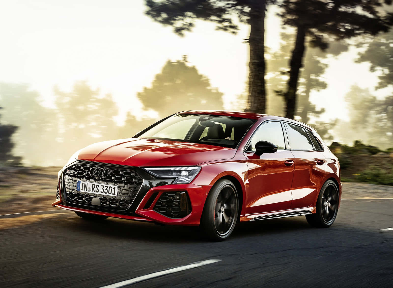 紅色 Audi RS3 Sportback 在陽光明媚的道路上行駛，背景有樹木。
