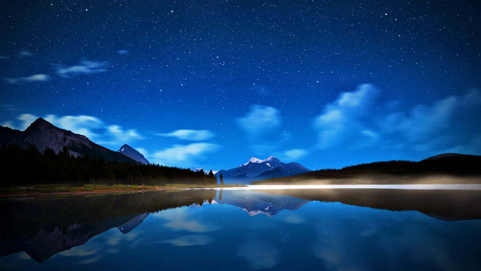 湖畔高解析度夜空 壁紙 — 星空夜空完美地倒映在平靜的湖面上，四周環繞著黑暗的山脈和樹木。